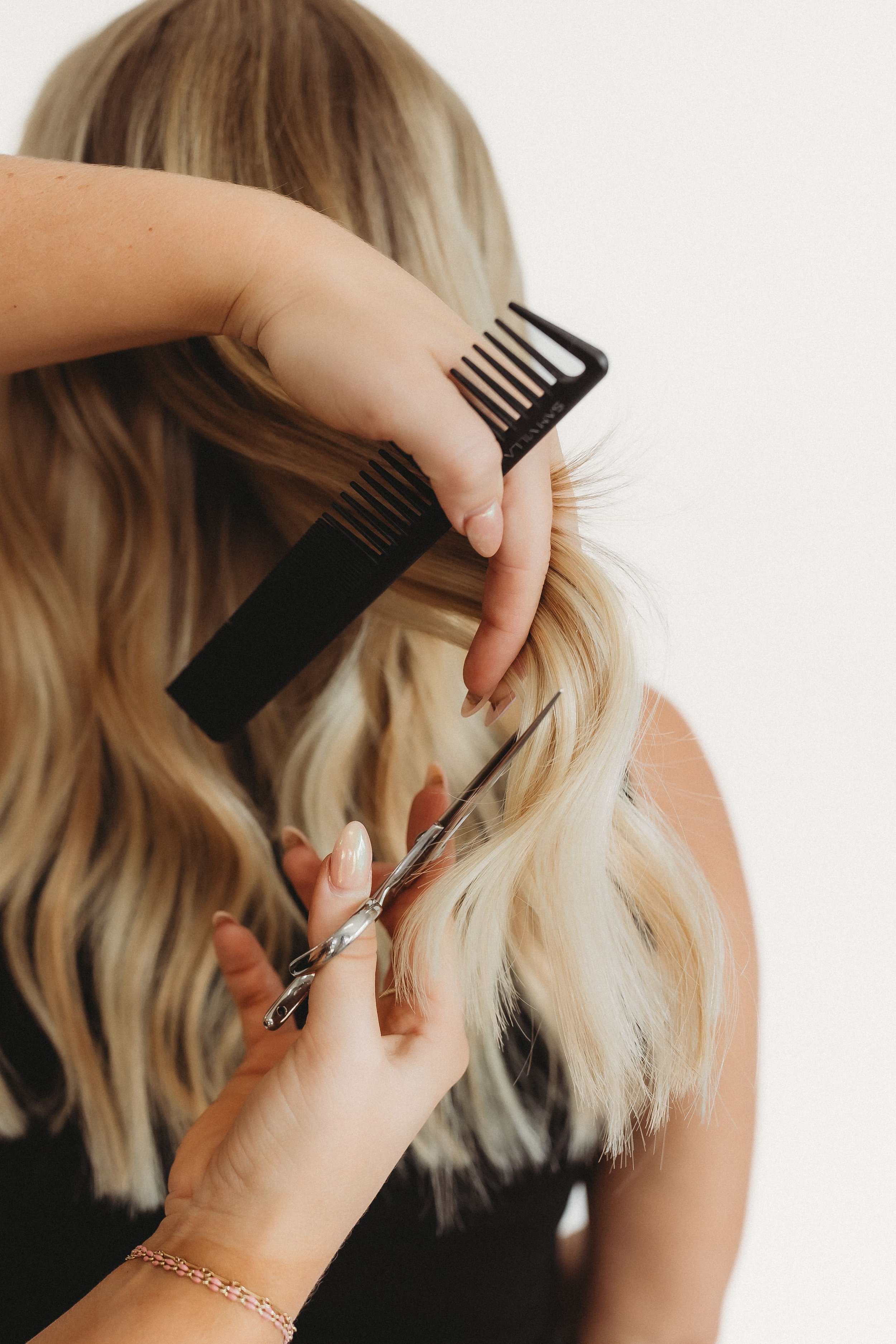  during a stylist photoshoot, a pair of hands hold a comb ands sheers to a woman’s head of hair 
