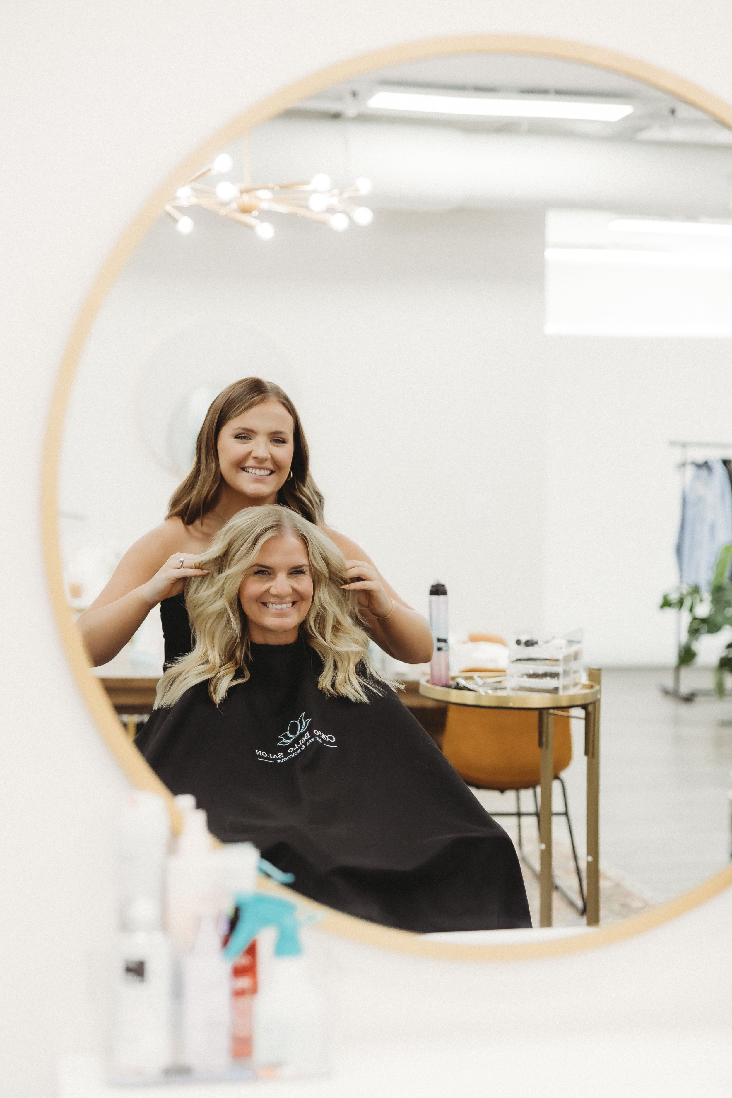  a hair stylist and her client smile together as she fluffs her hair during a stylist photoshoot 