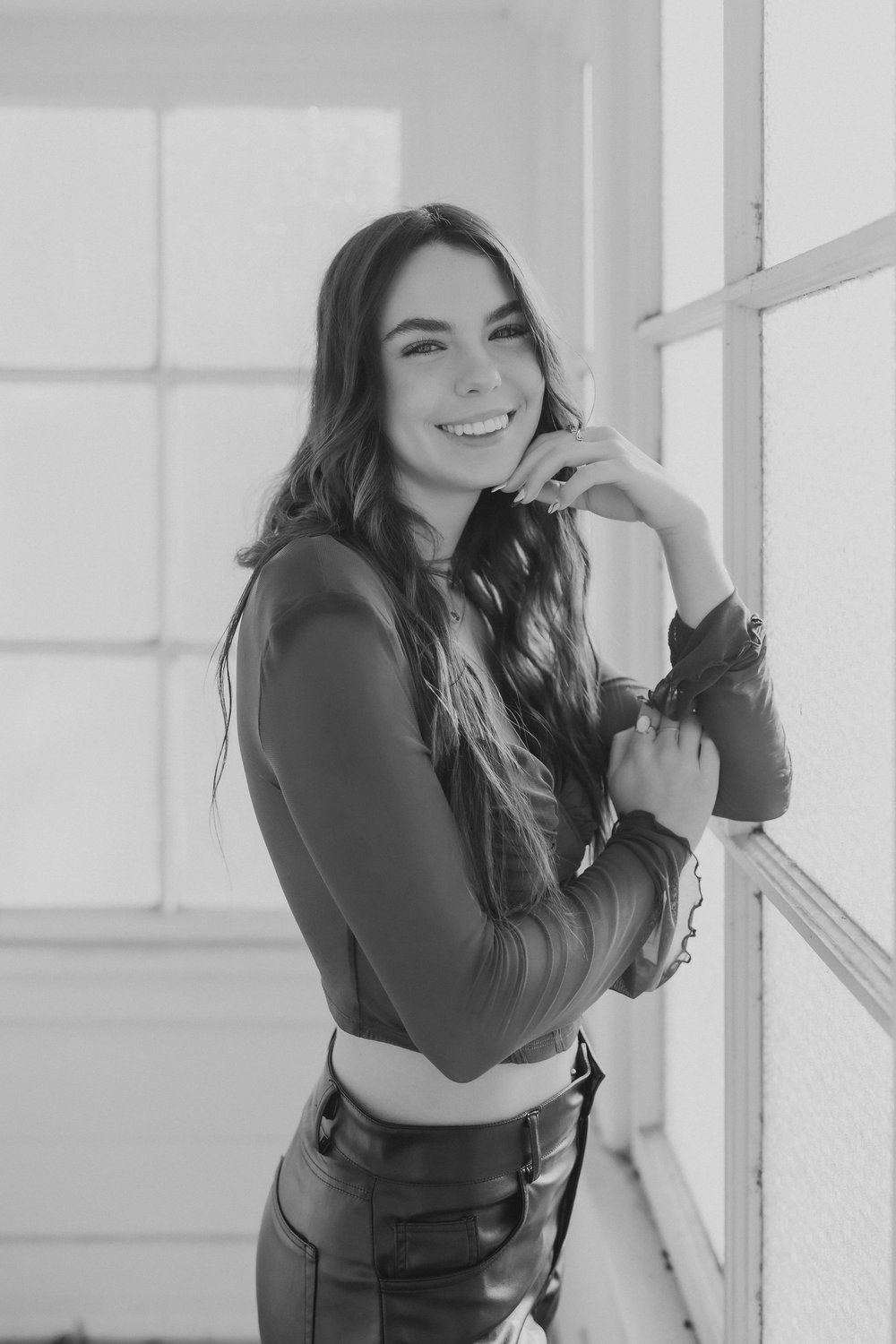  a teenage girl smiles for a senior photos photographer with one arm crossed across her chest and the other supporting her face 