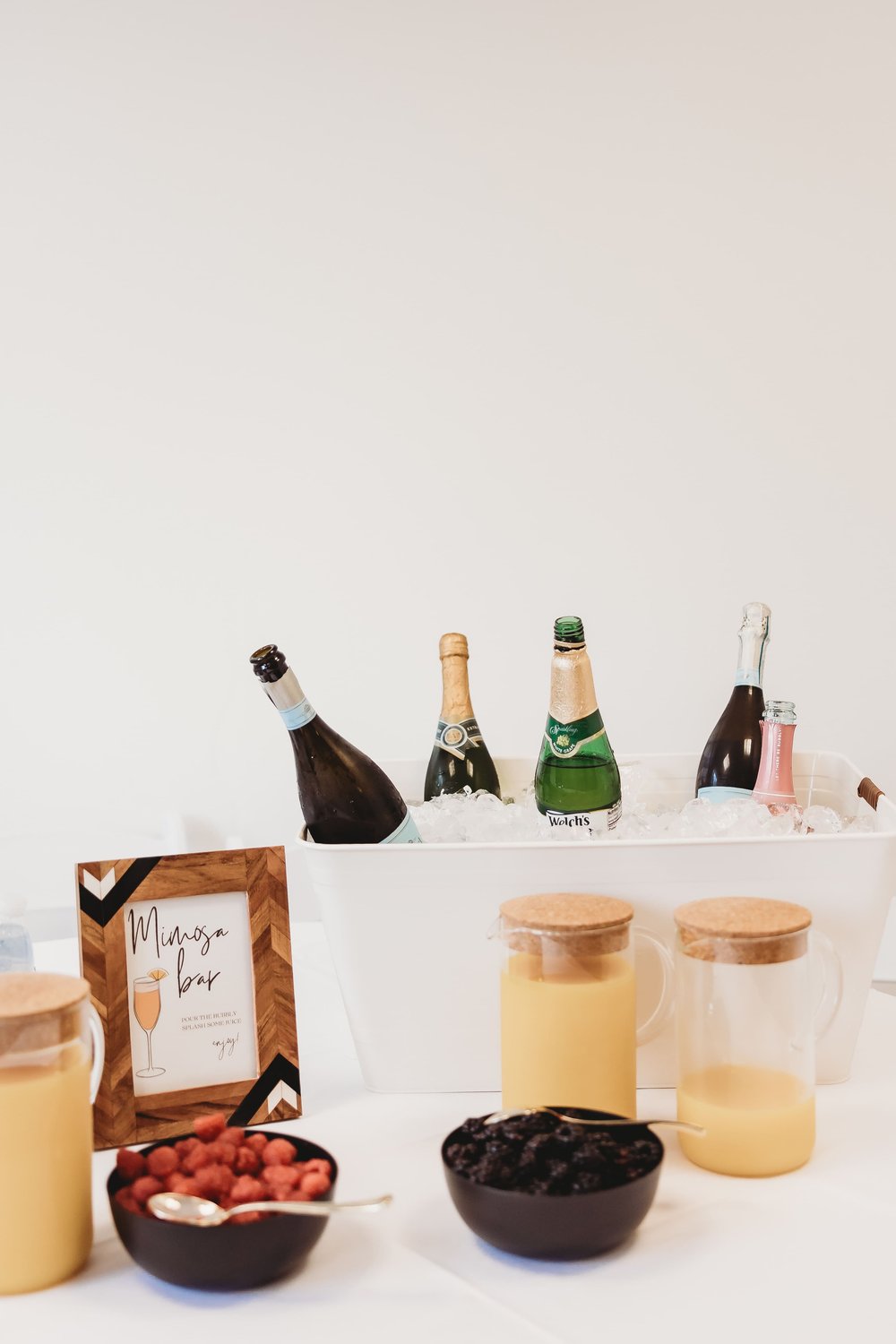  a photo of the mimosa bar at a bridal shower—bottles on ice, raspberries in a bowl, containers of orange juice 