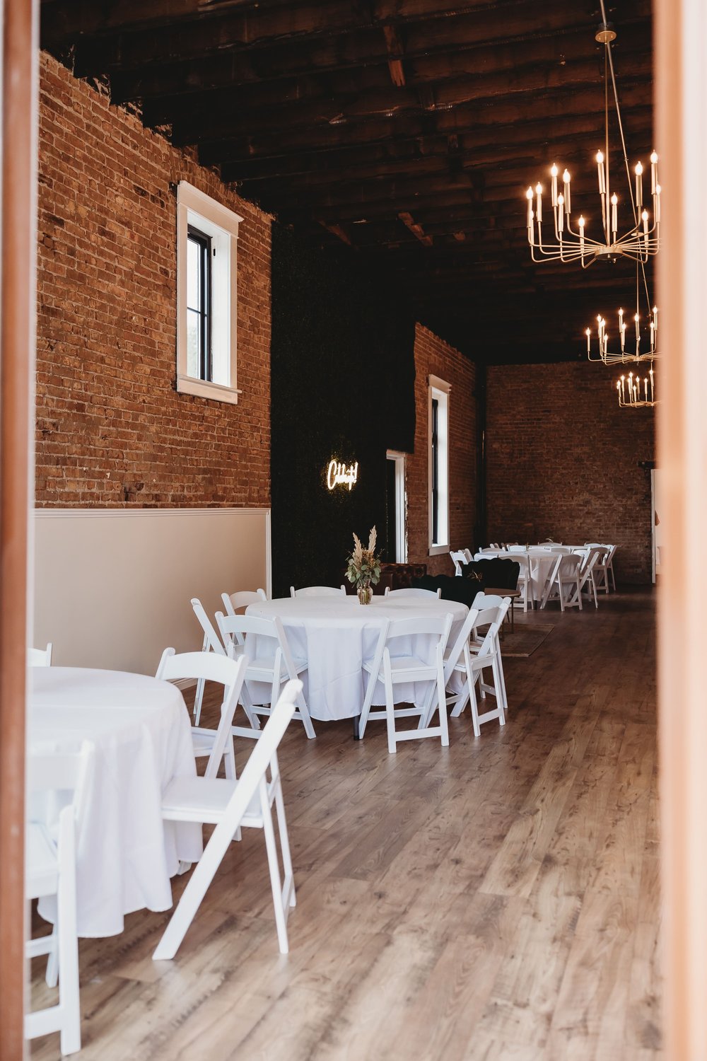  from the doorframe we see three round tables with white tablecloths and white wooden folding chairs  