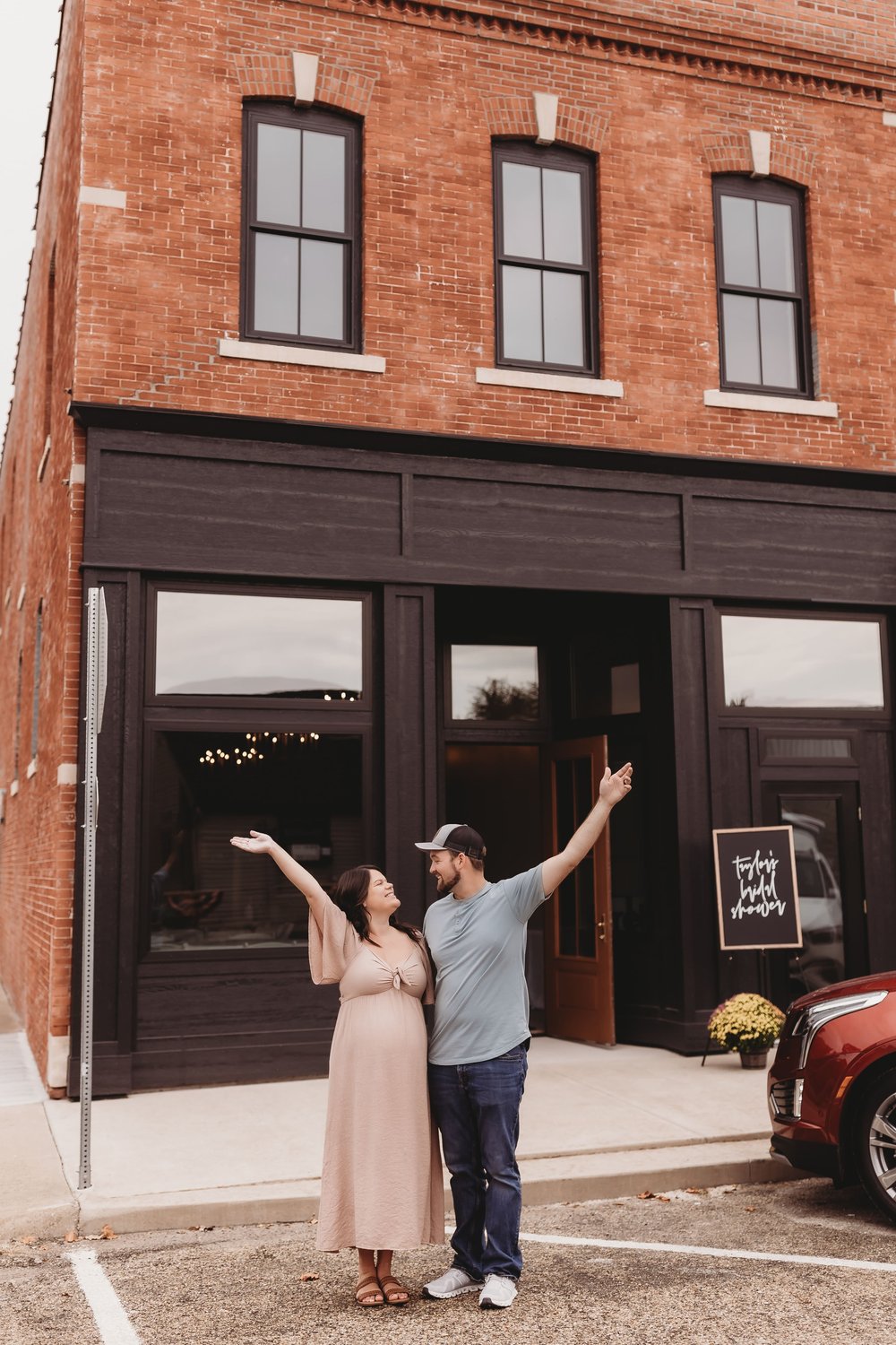  a husband and wife duo stand outside of their business for their brand photos with their arms in the air 