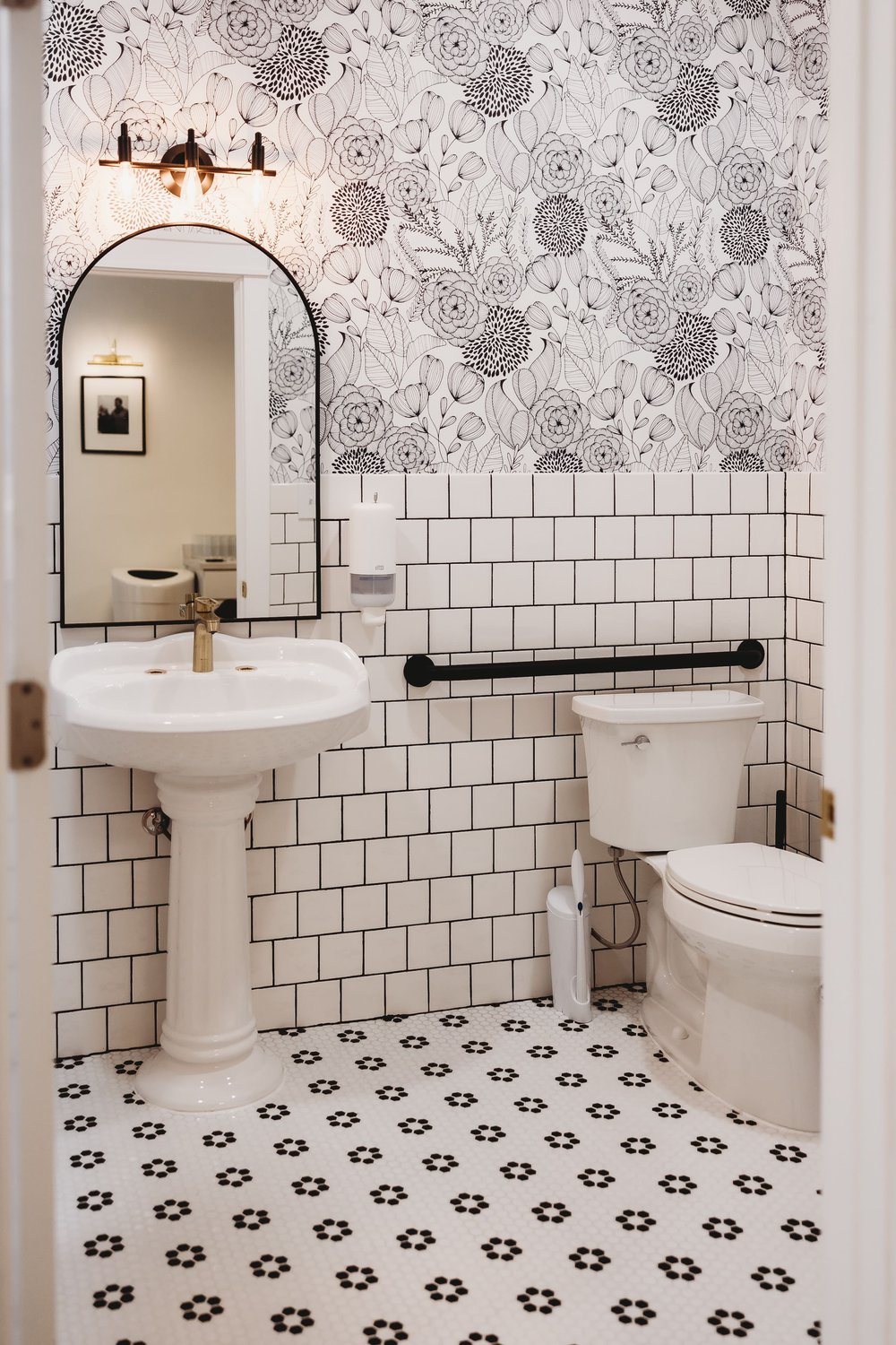  a white floral updated bathroom with an arched mirror and pedestal sink 
