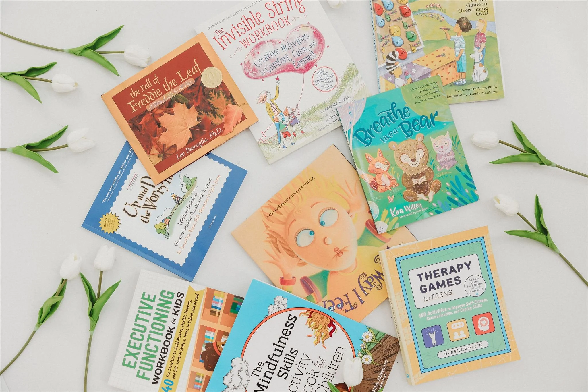 A flat lay of children's mental health and therapy books surrounded by white tulip stems.