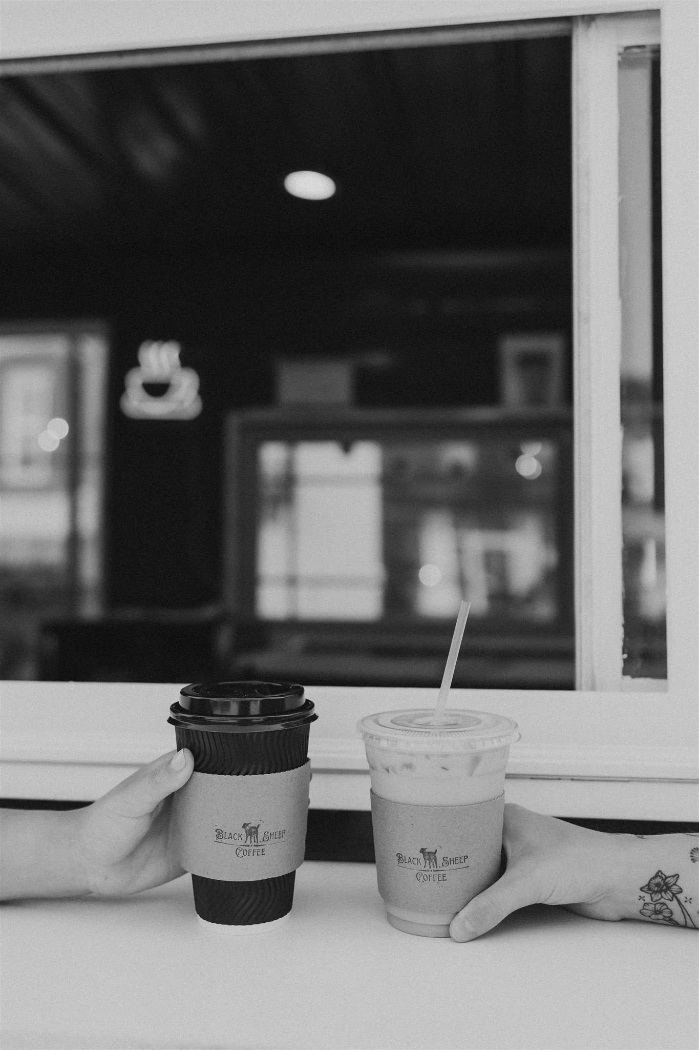 Two hands holding coffee cups on a counter, with a window behind them, in black and white.