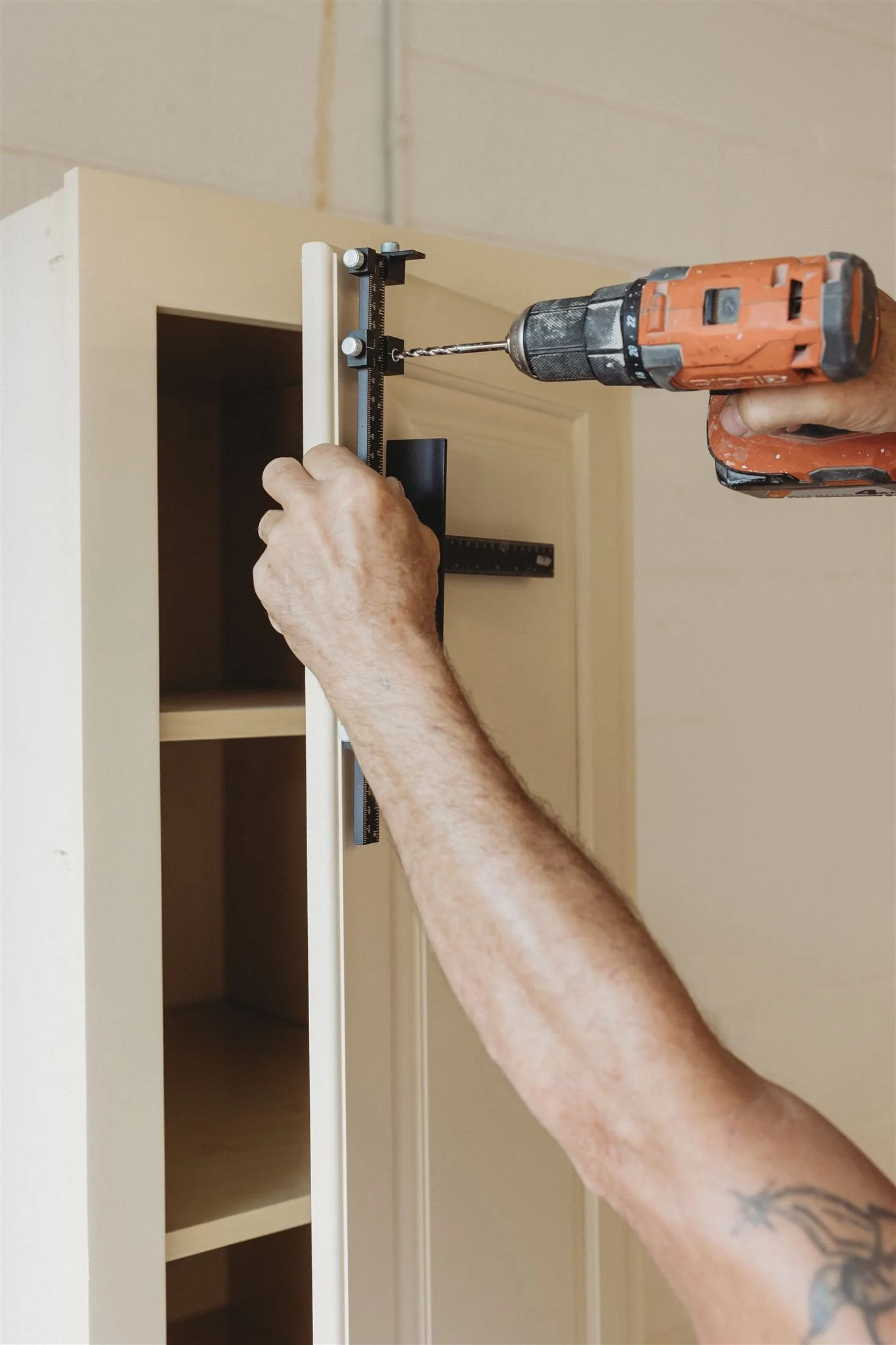 Person using a cordless drill to install a vertical white trim piece on a wooden cabinet or shelf.