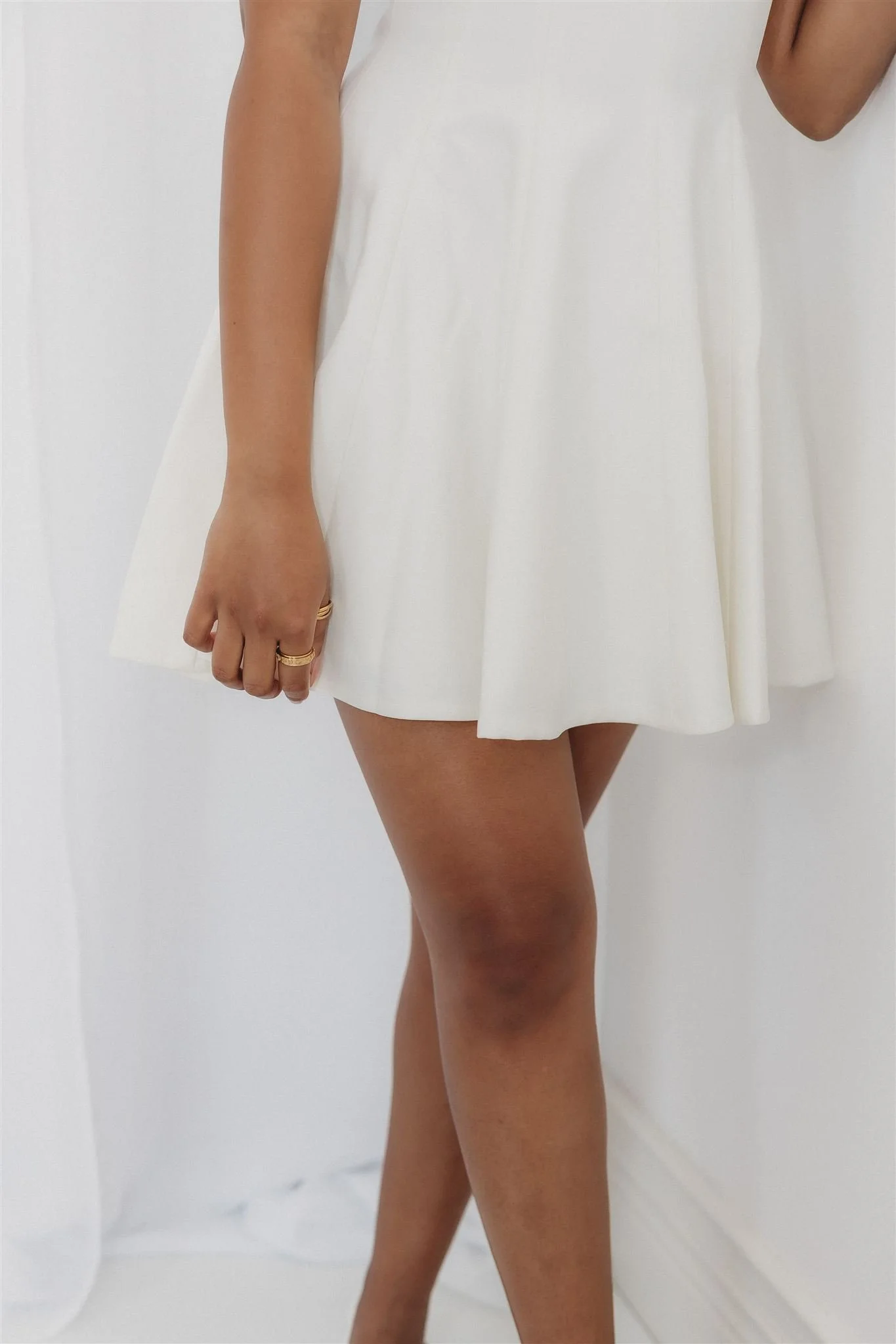 A woman wearing a white dress, showing her arm, hand, and leg, standing against a white background.