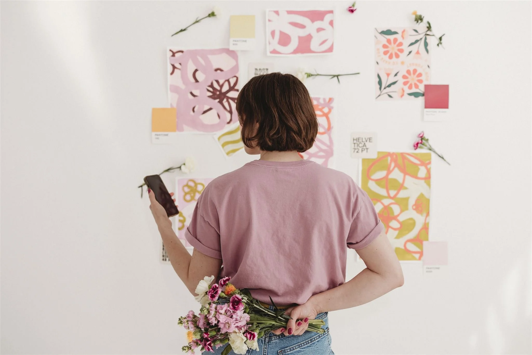 A Blooming Design Co. brand designer reviewing a colorful floral-inspired mood board featuring Pantone swatches, typography samples, and botanical illustrations, capturing the creative brand strategy and visual identity design process.