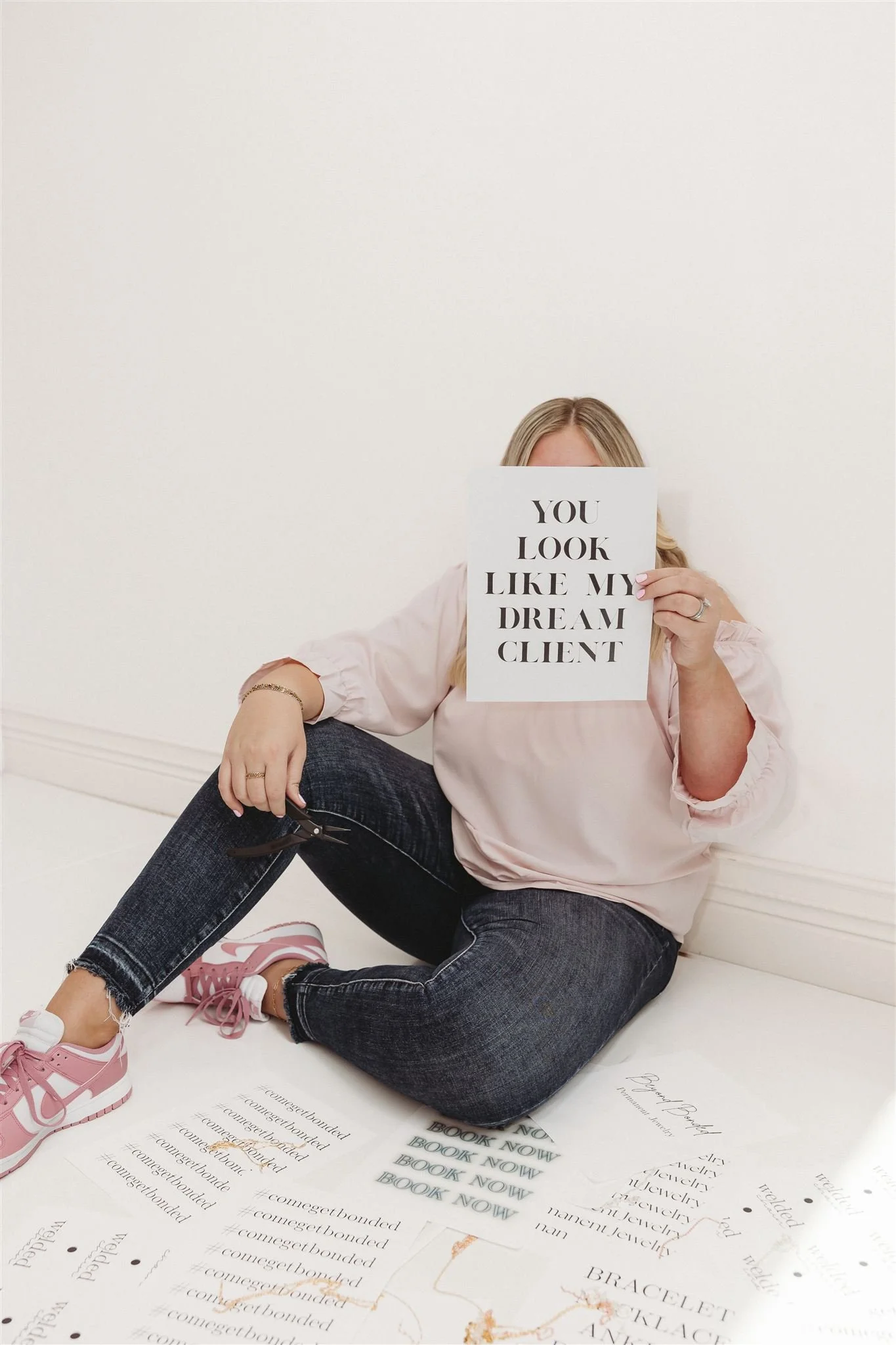 Woman sitting on the floor holding a sign that says "You look like my dream client" in front of her face. There are papers with text on the floor nearby.