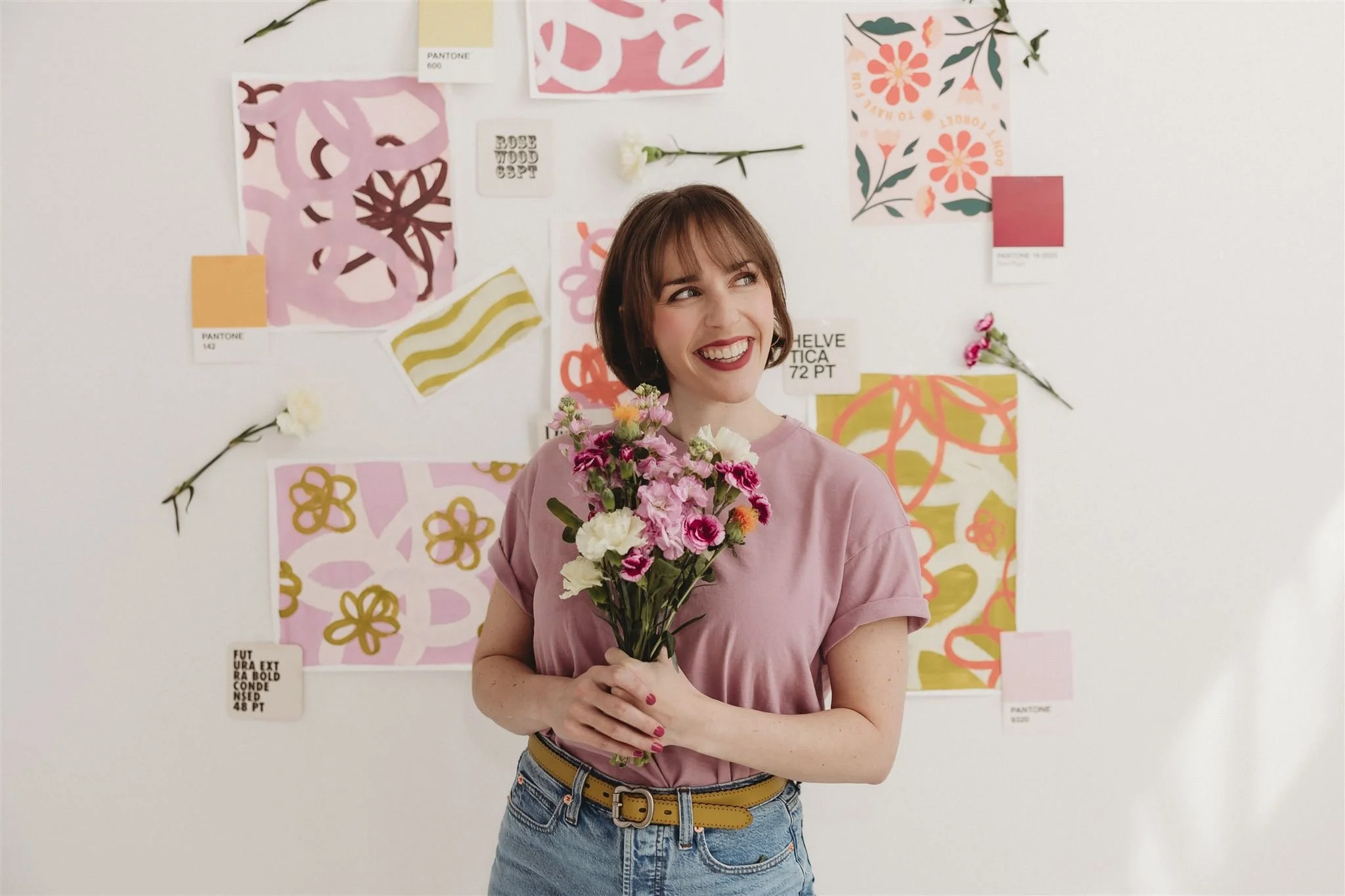 Claire, founder of Blooming Design Co., smiling and holding a bouquet of flowers in front of a vibrant brand mood board featuring Pantone swatches, floral illustrations, and typography samples