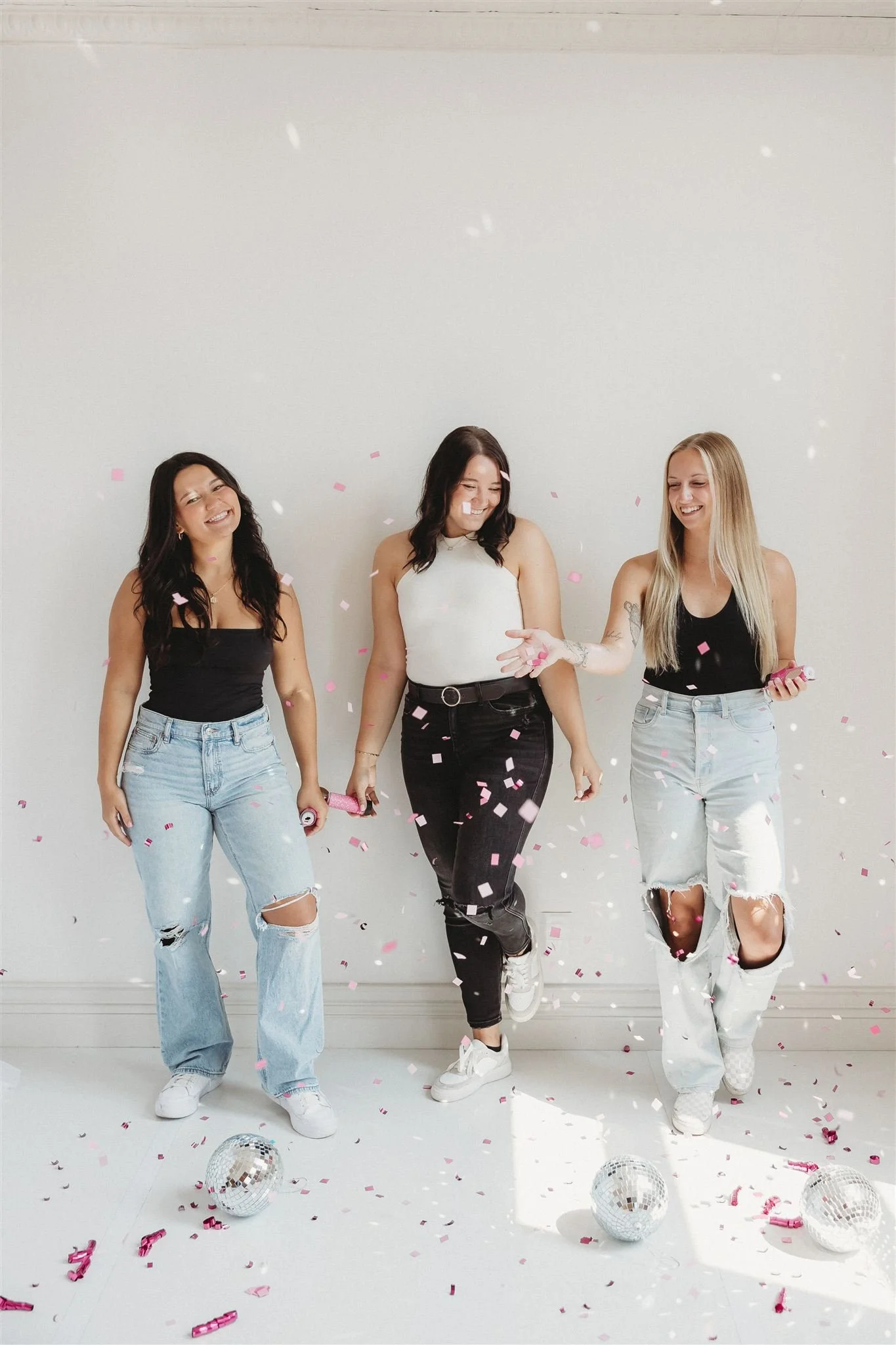 Three women celebrating with confetti and disco balls on the floor, smiling and enjoying the moment.