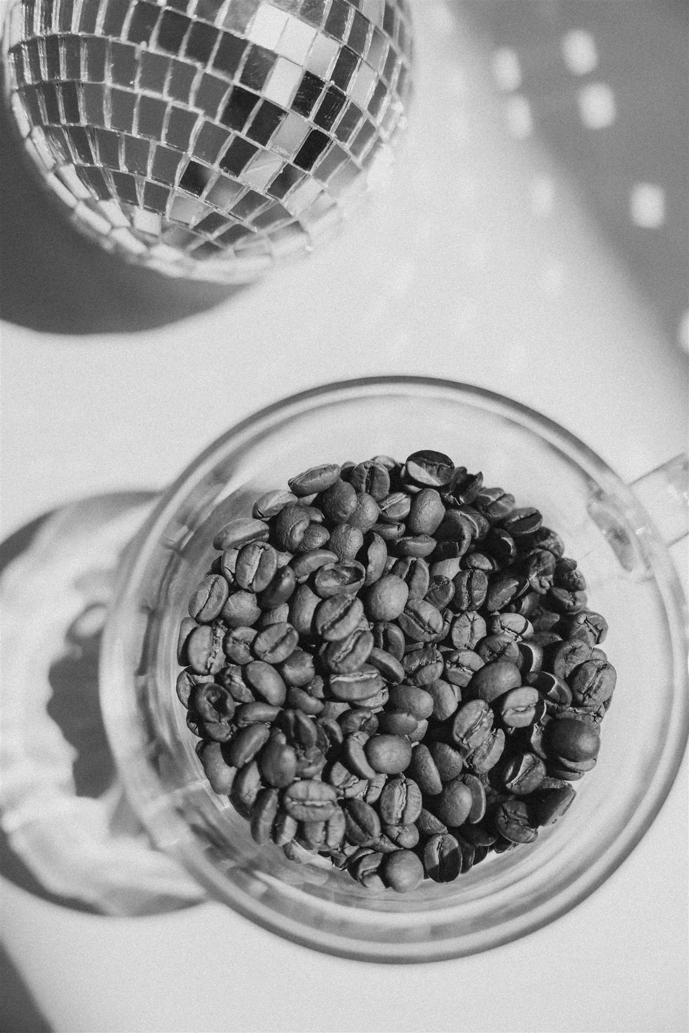 A glass jar filled with roasted coffee beans and a disco ball reflecting light in the background.