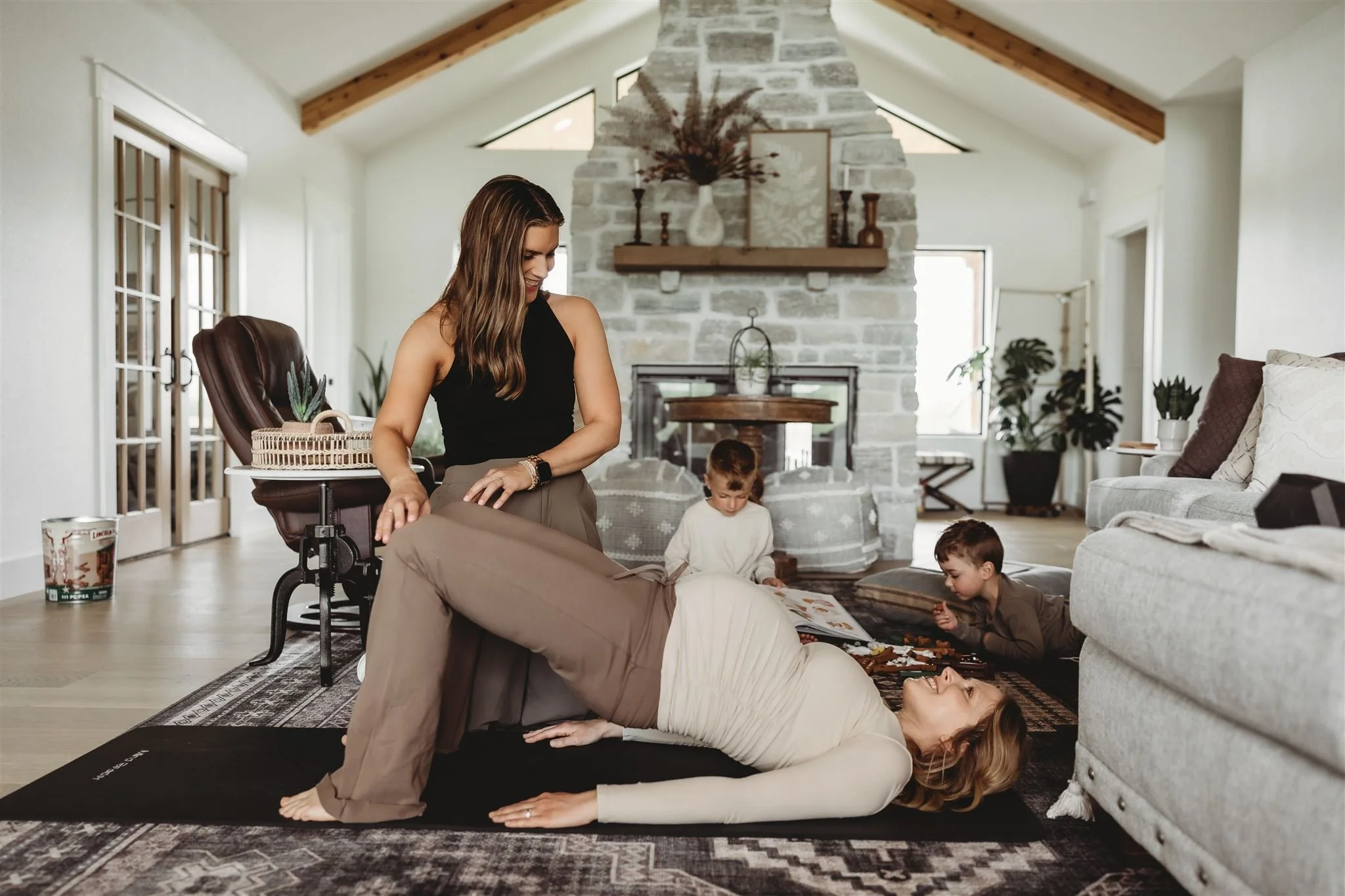 Physical therapist performs in-home prenatal physical therapy with a pregnant woman lying on a yoga mat, while her children play nearby, showcasing family-friendly mobile physiotherapy and pregnancy rehabilitation services.