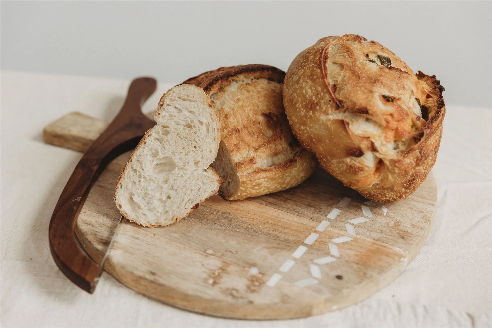 Sliced sourdough boule and herb bread roll on a wooden cutting board — Wild Flour Sourdough Bakehouse brand photography, Central Illinois