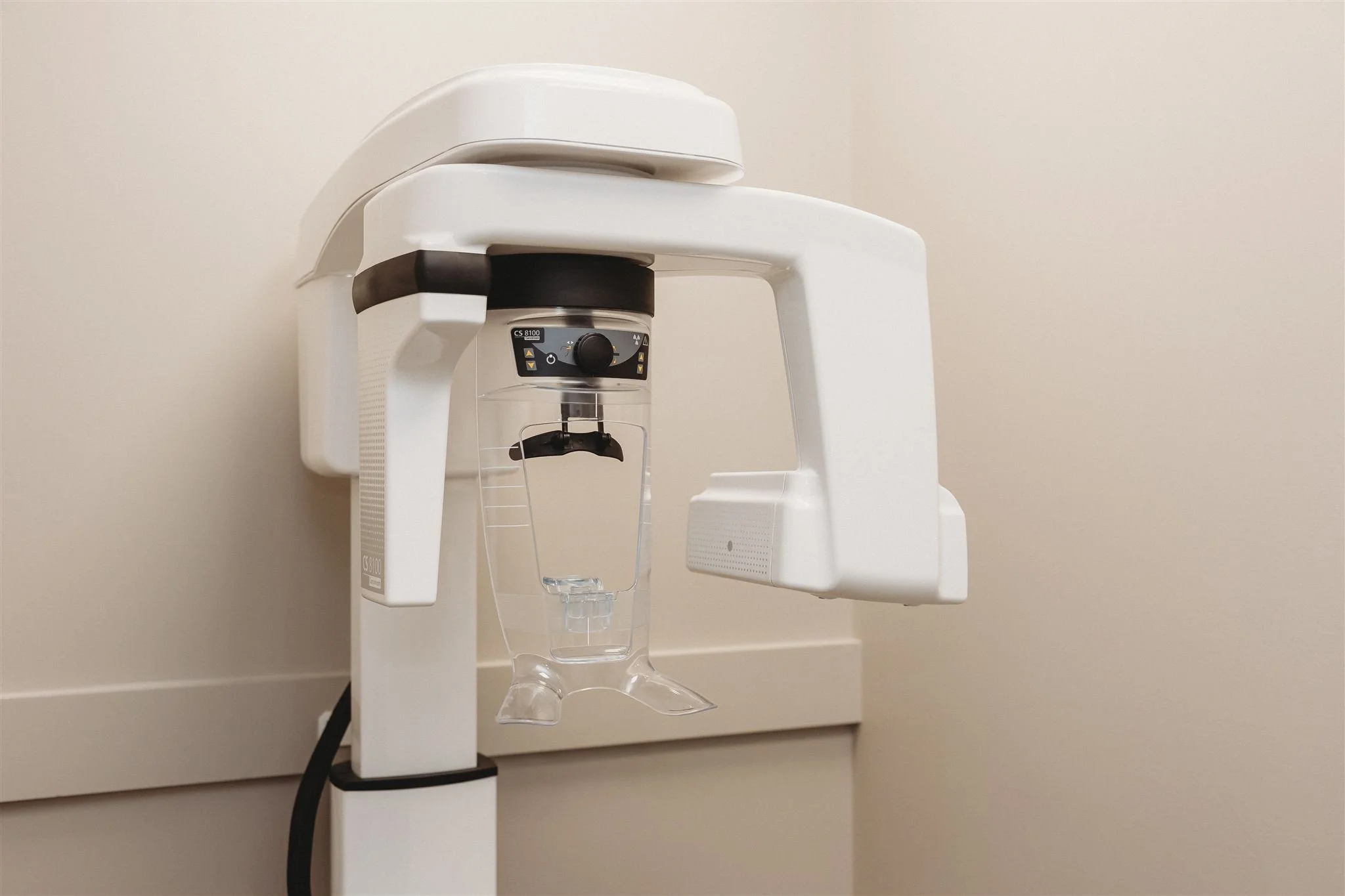 A dental X-ray machine mounted on a beige wall in a dental office.
