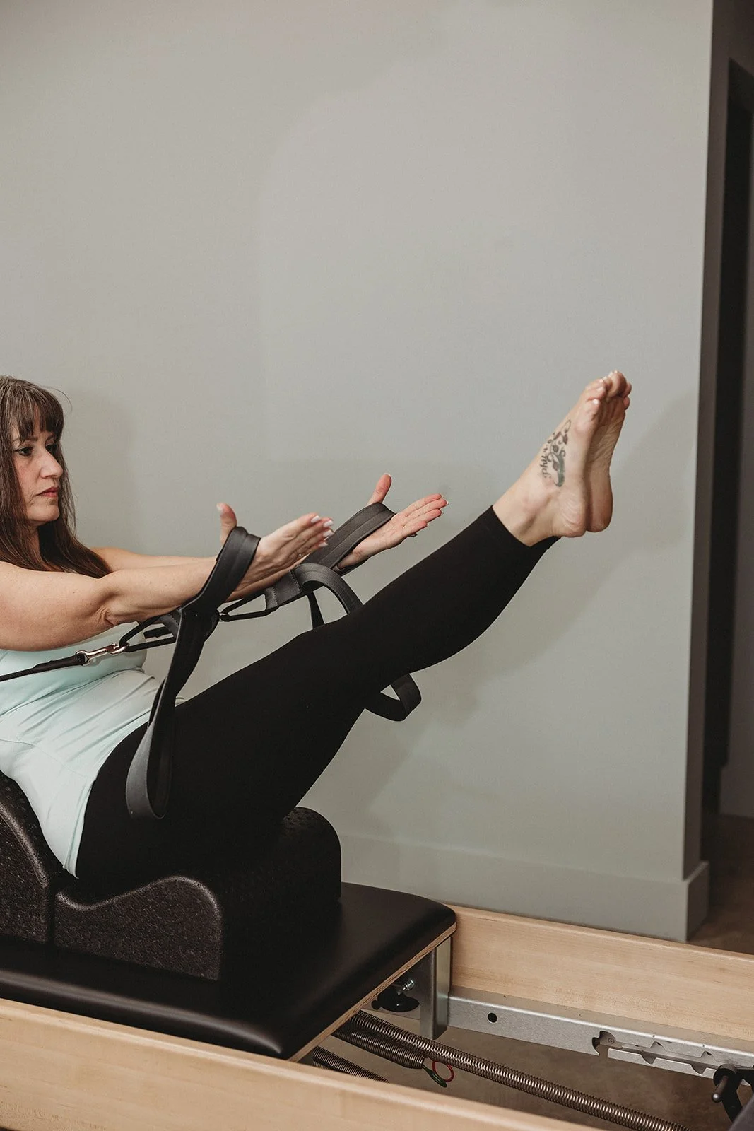 A woman doing a leg lift exercise in a specialized fitness equipment, with her arms positioned in front of her for balance, in a room with plain walls.