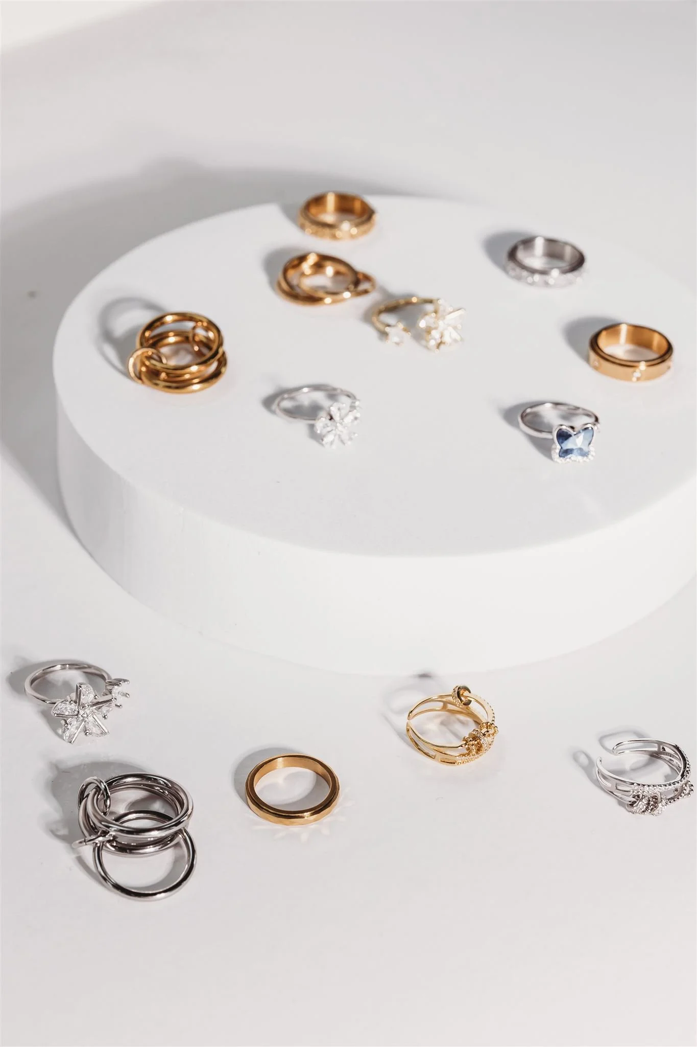 Various gold and silver rings, some with gemstones, displayed on a white circular platform and a white surface.