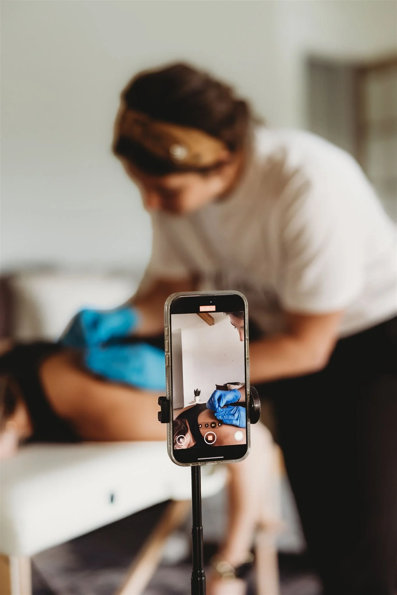 A Vitality Physical Therapy and Wellness physiotherapist performing a hands-on dry needling or manual therapy treatment while recording the session on a smartphone