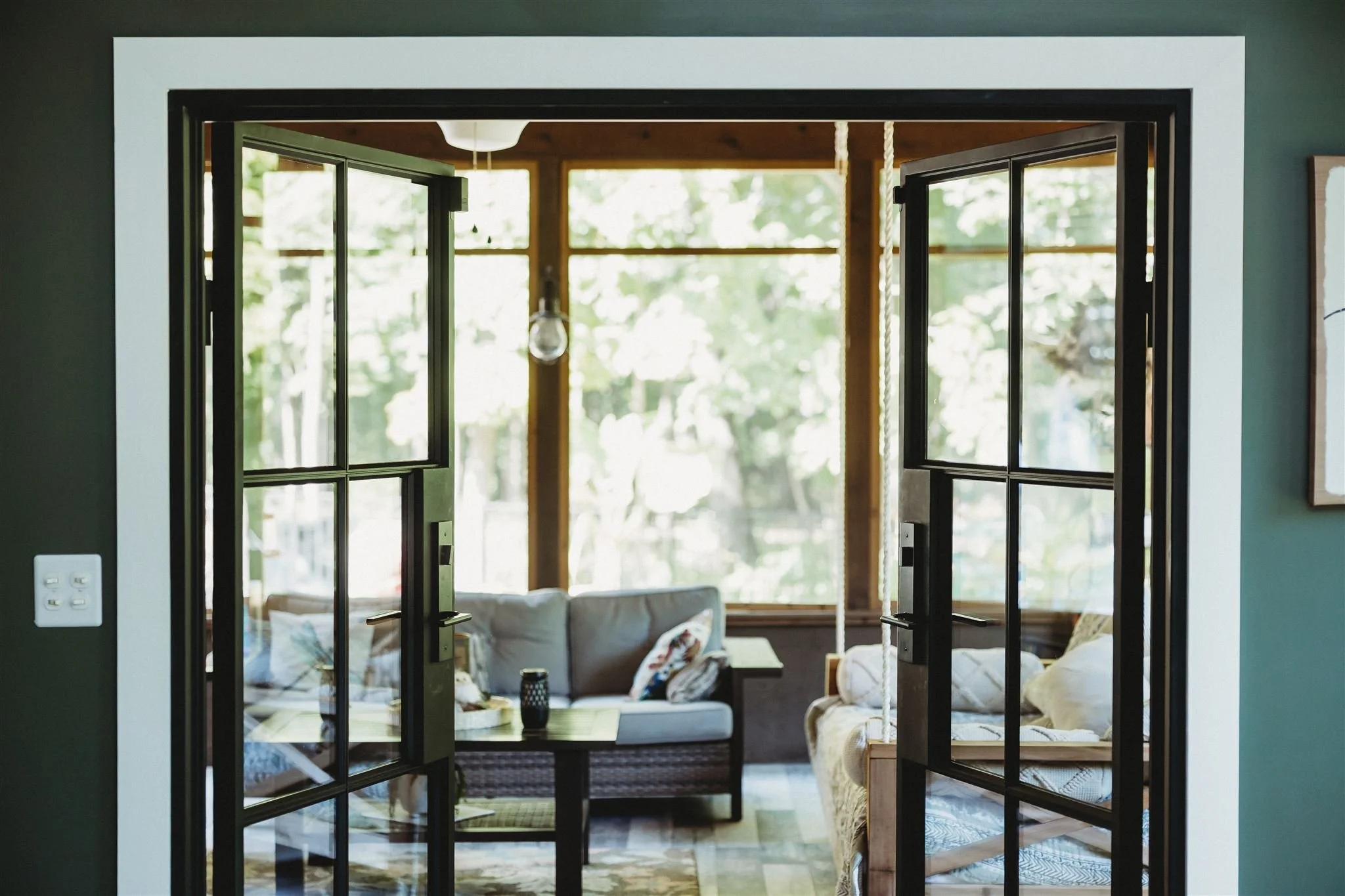 Custom black French doors crafted by Walters Woodworking opening into a sunlit screened porch, showcasing their precision millwork and custom door installation for residential home renovation and outdoor living spaces.