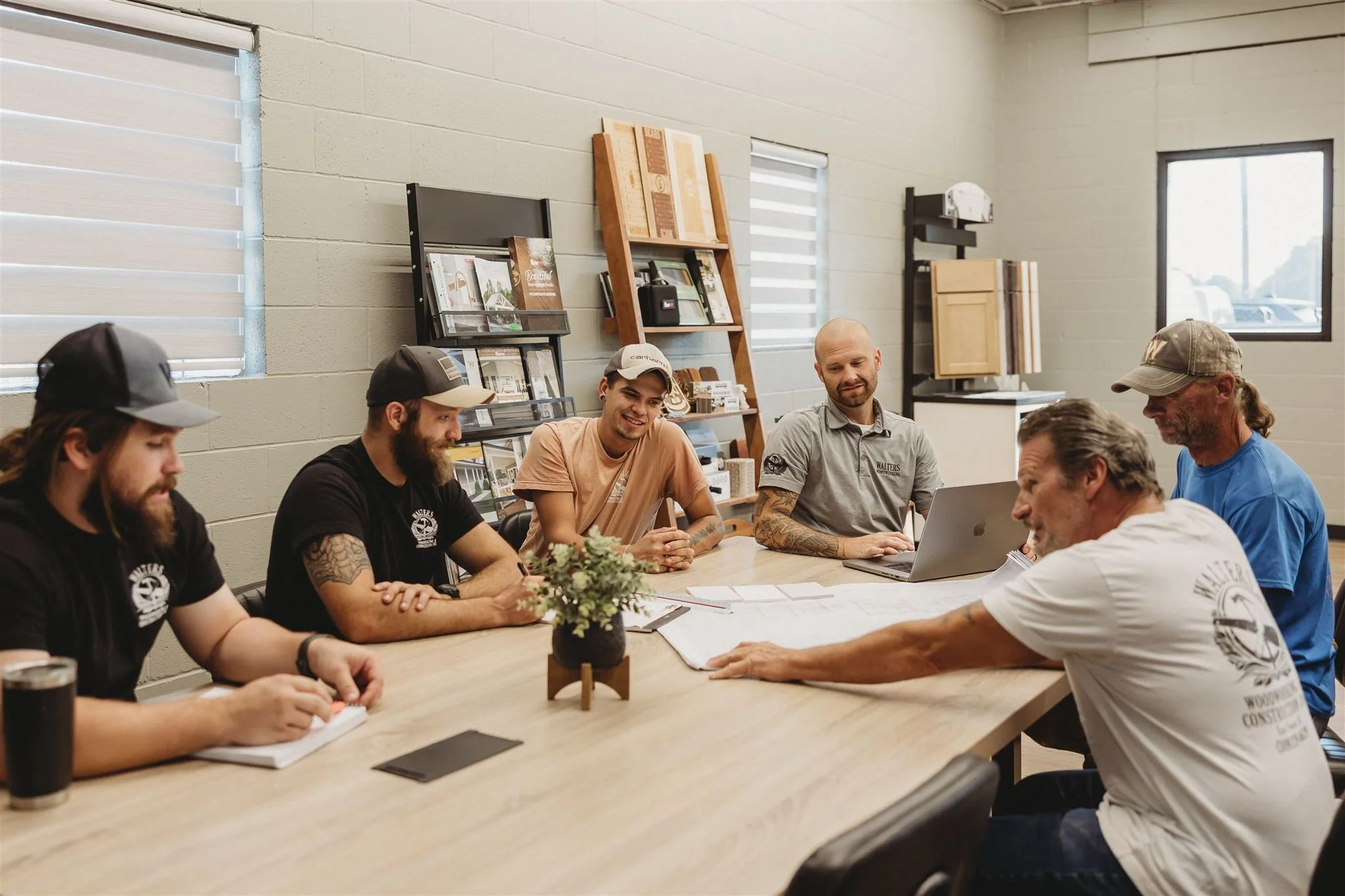 The Walters Woodworking team collaborating around a conference table in their showroom, surrounded by wood samples and cabinetry displays, showcasing their dedicated craftsmen and commitment to custom woodworking project planning.
