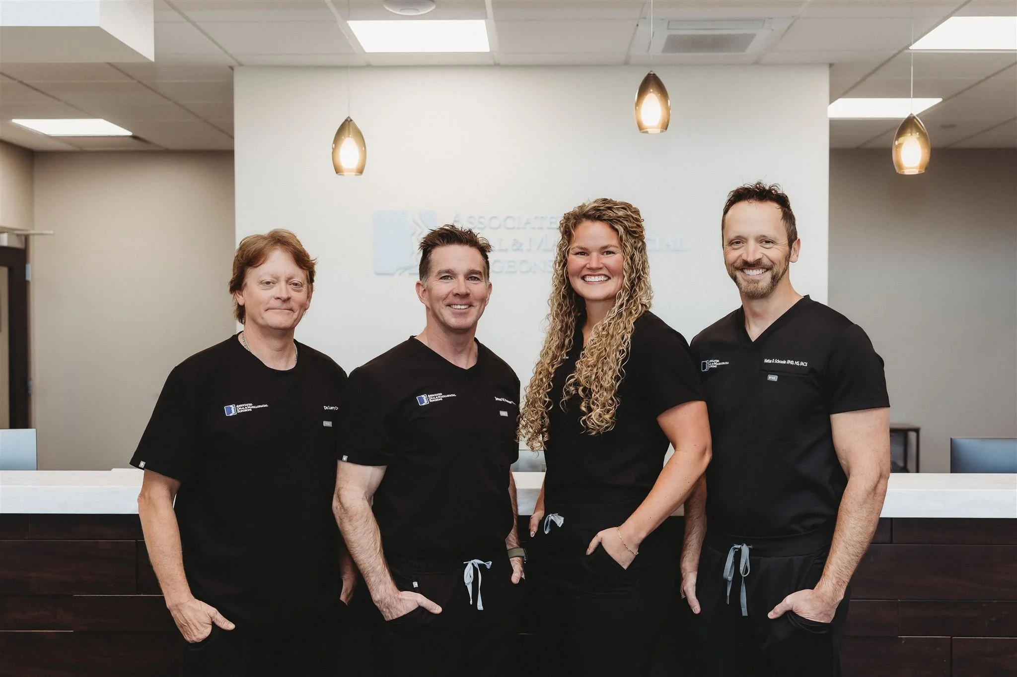 Four healthcare professionals standing behind a reception desk in an office, smiling for the camera.