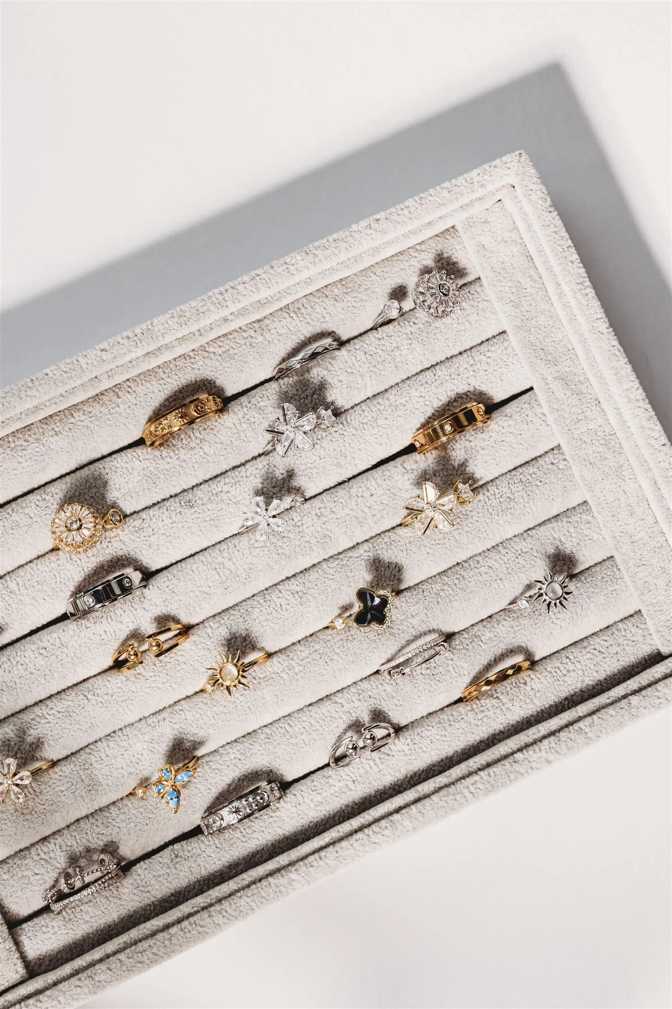 A display box of various rings, including gold, silver, and black designs with different gemstone accents and shapes.