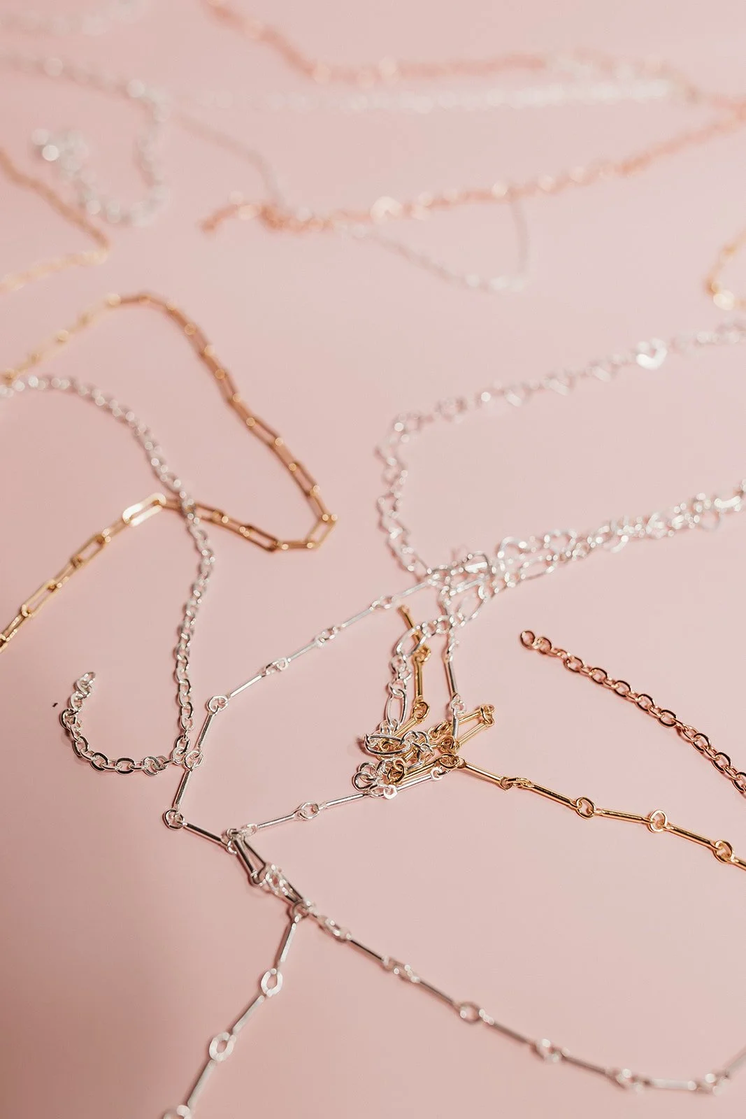 Various delicate necklaces in gold and silver colors scattered on a pink background.