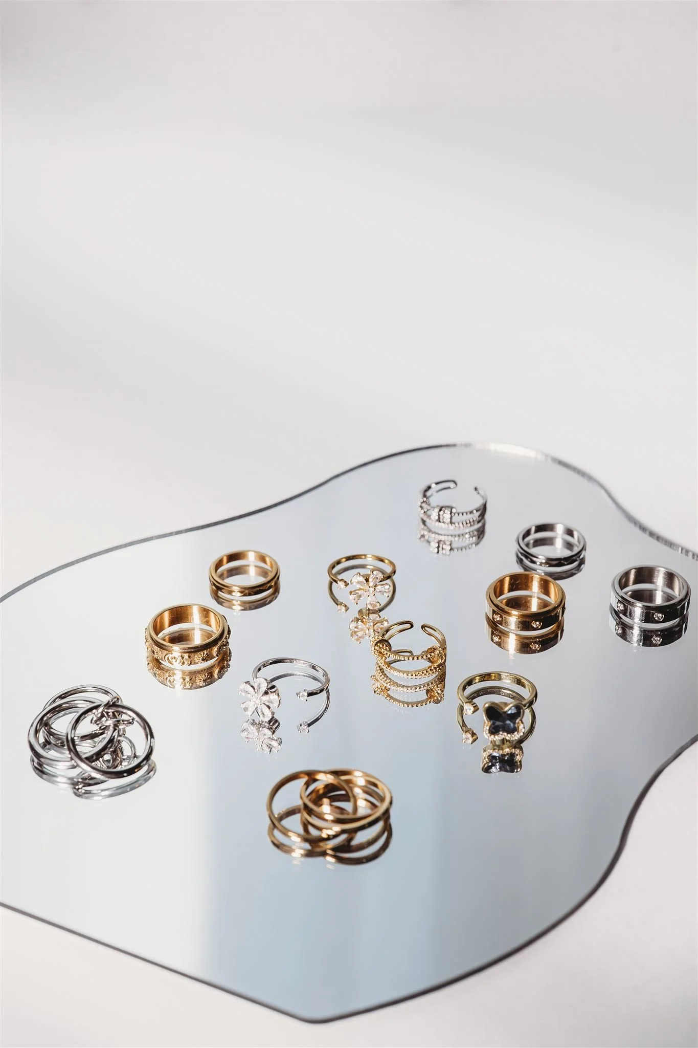 Various rings, including gold and silver, displayed on a reflective surface with a white background.