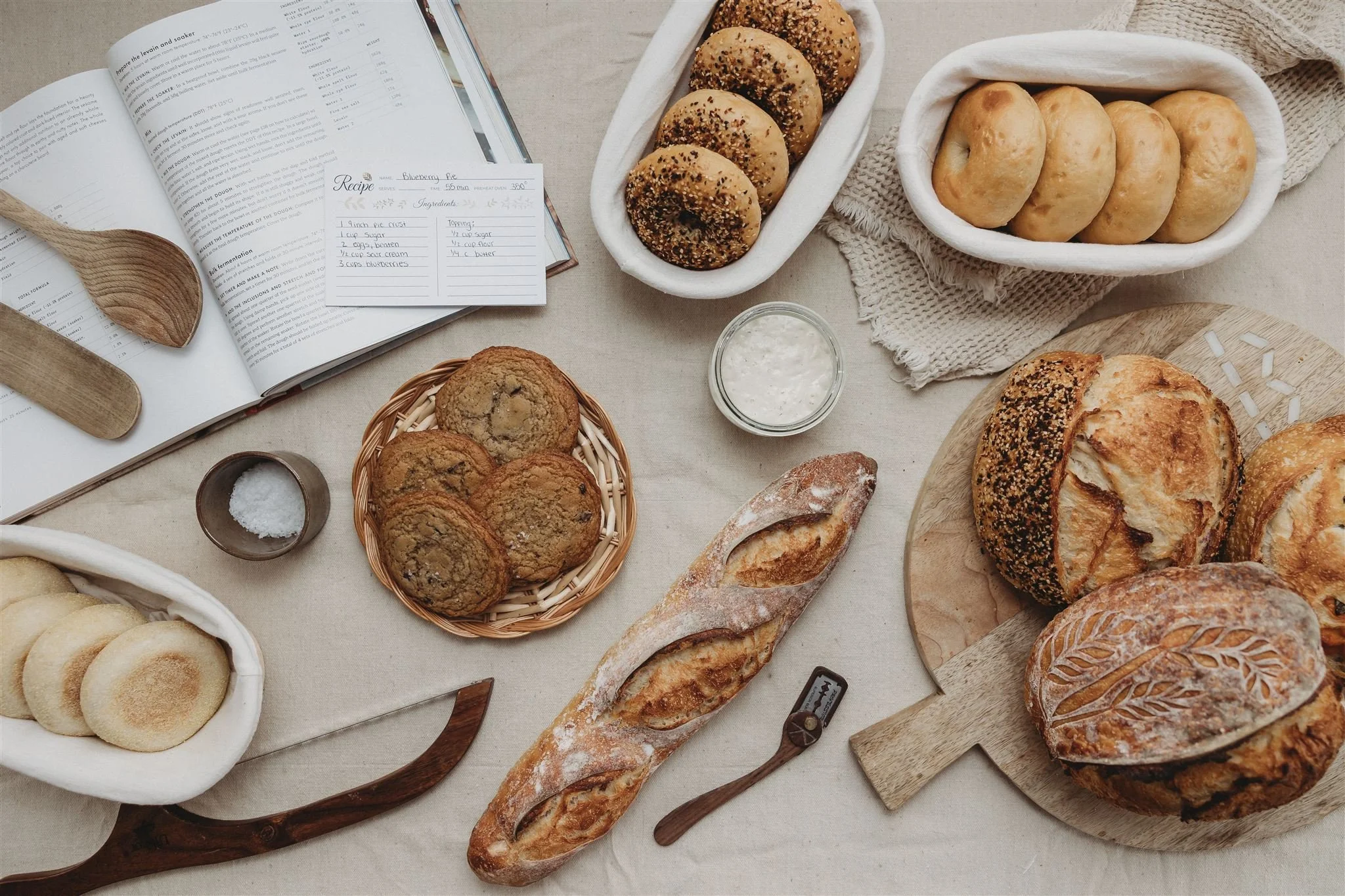 Brand photo of Wild Flour Sourdough Bakehouse market display featuring artisan breads and croissants on a wooden bakery rack, kraft paper packaging, baby's breath florals, and a linen branded tablecloth — Central Illinois brand photography