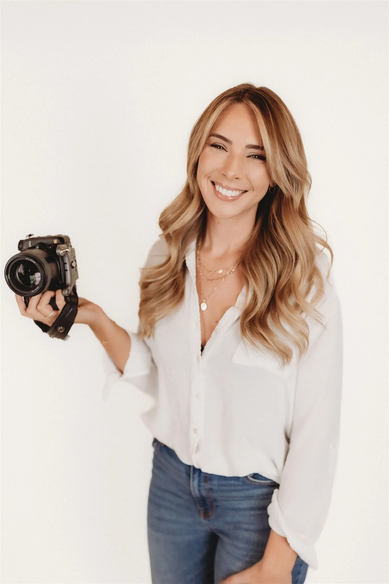 a photographer smiles for a headshot with a camera in her hand