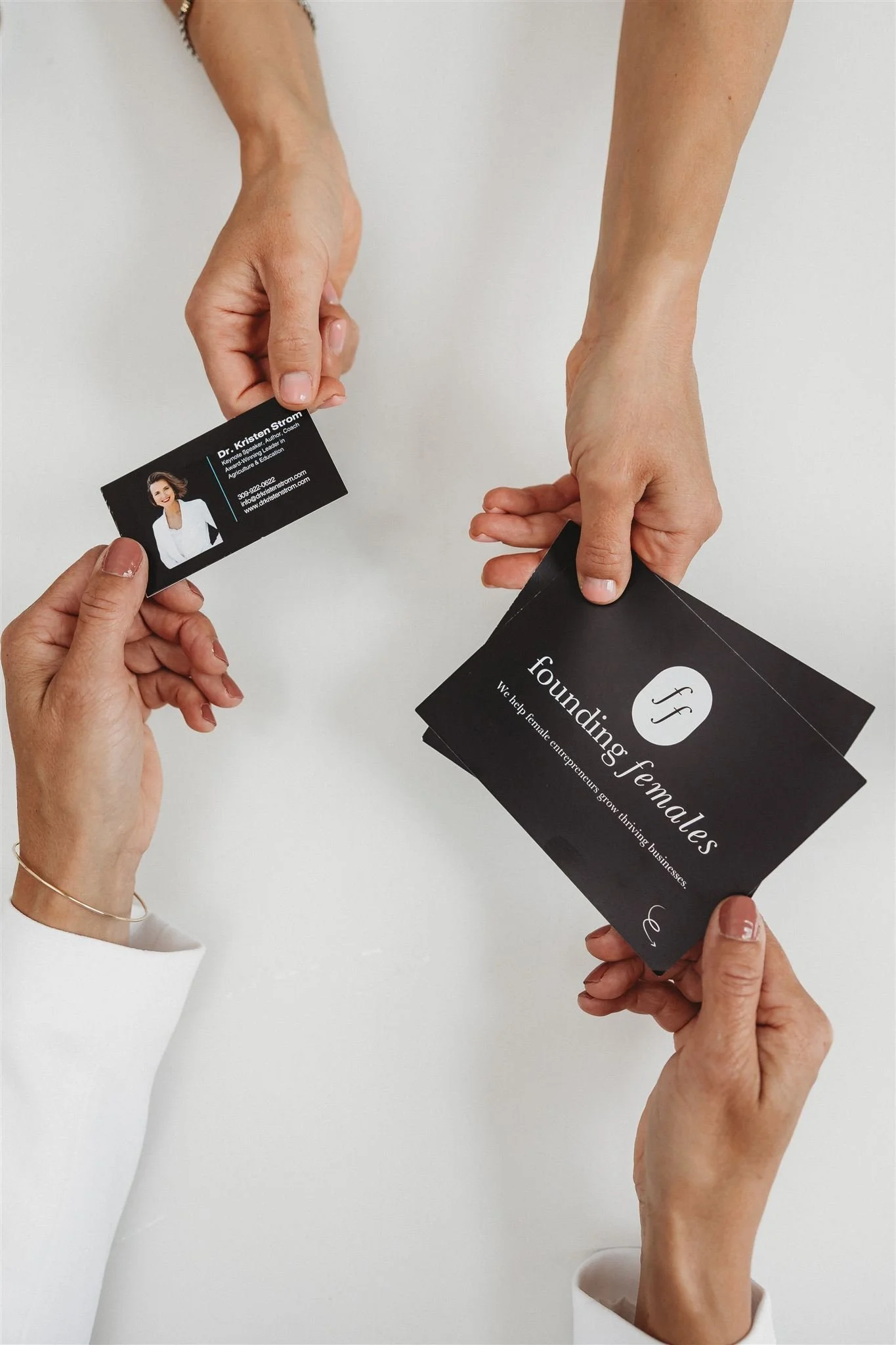 Two women exchanging business cards. One woman has a business card with her photo and contact information; the other is holding a stack of cards with the logo and text 'foundings females'.