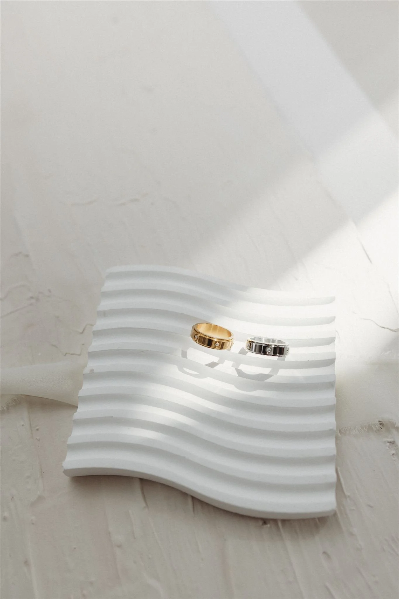 Gold and silver rings with embedded diamonds on a white textured display, against a white abstract background.