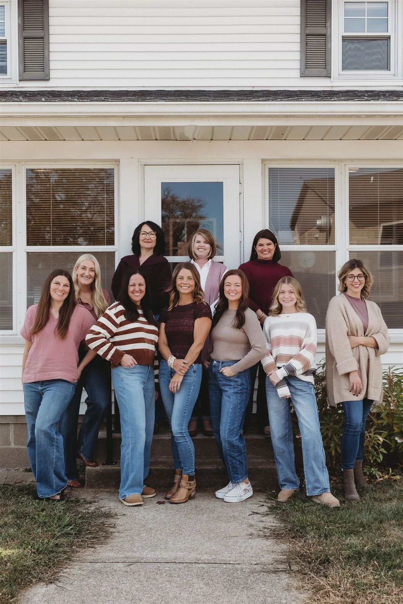 Group of ten women standing on steps in front of a house, smiling for a photo.