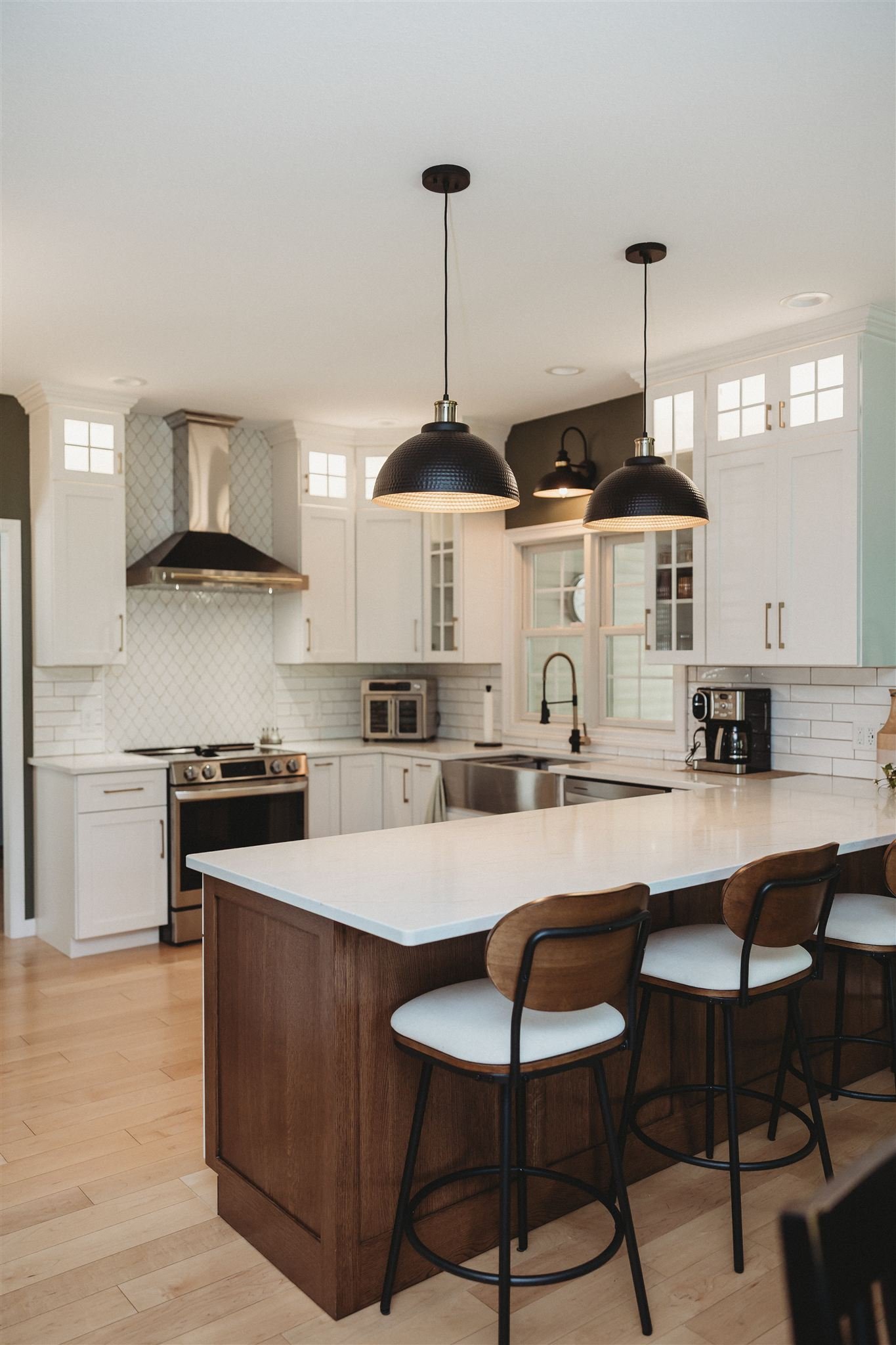 Modern kitchen with white cabinets, black pendant lights, wooden bar stools, and a white island counter.