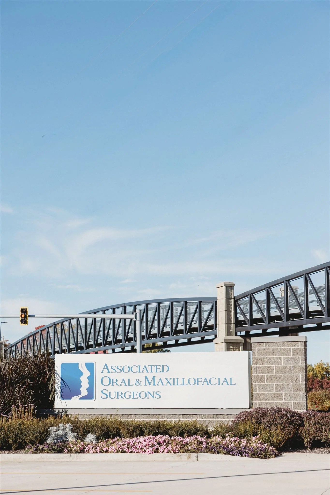 Sign for Associated Oral & Maxillofacial Surgeons in front of a landscaped area, with a building and clear sky in the background.