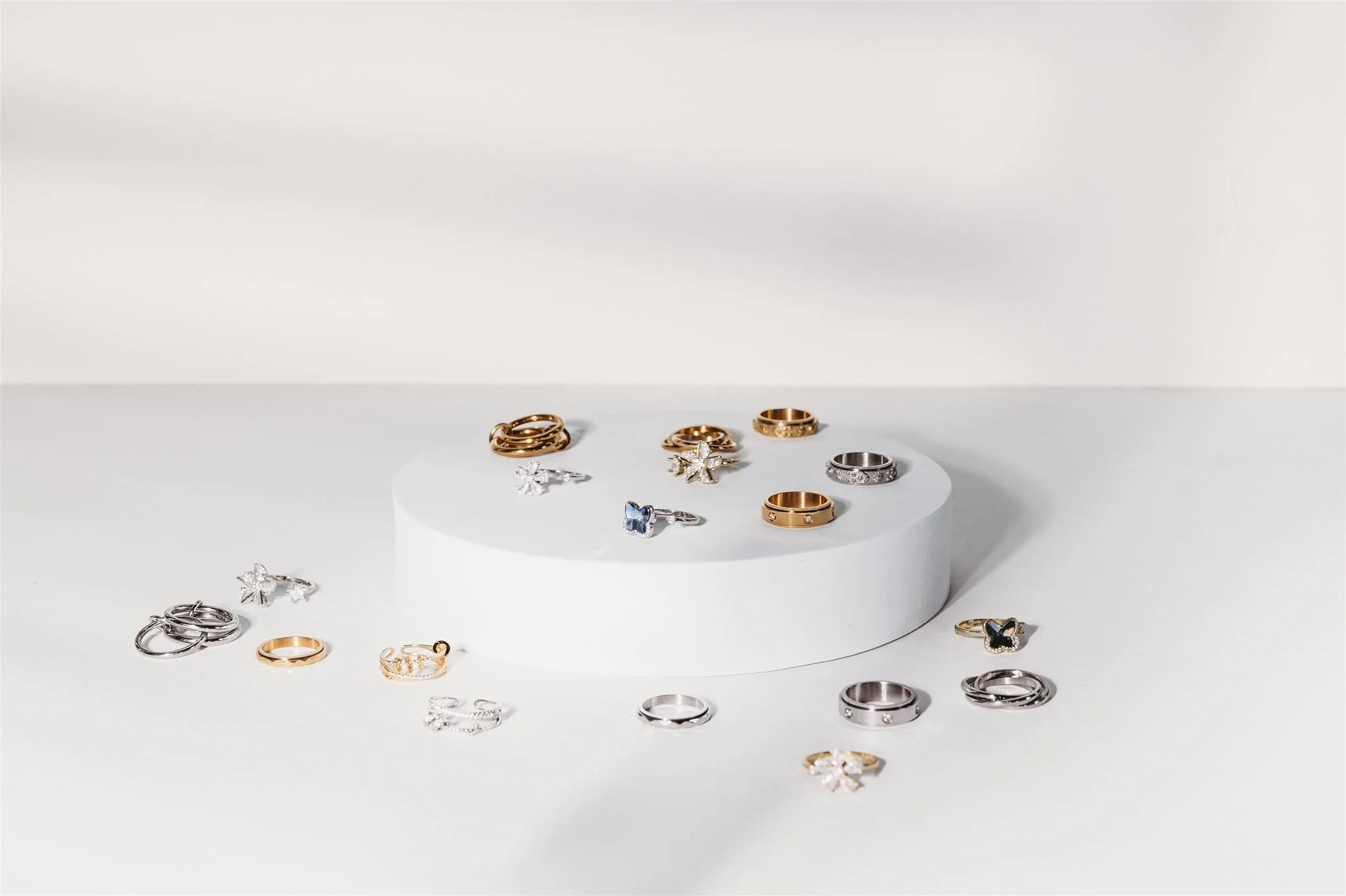 Display of various rings and earrings arranged on a white circular platform and white surface, with a white background.