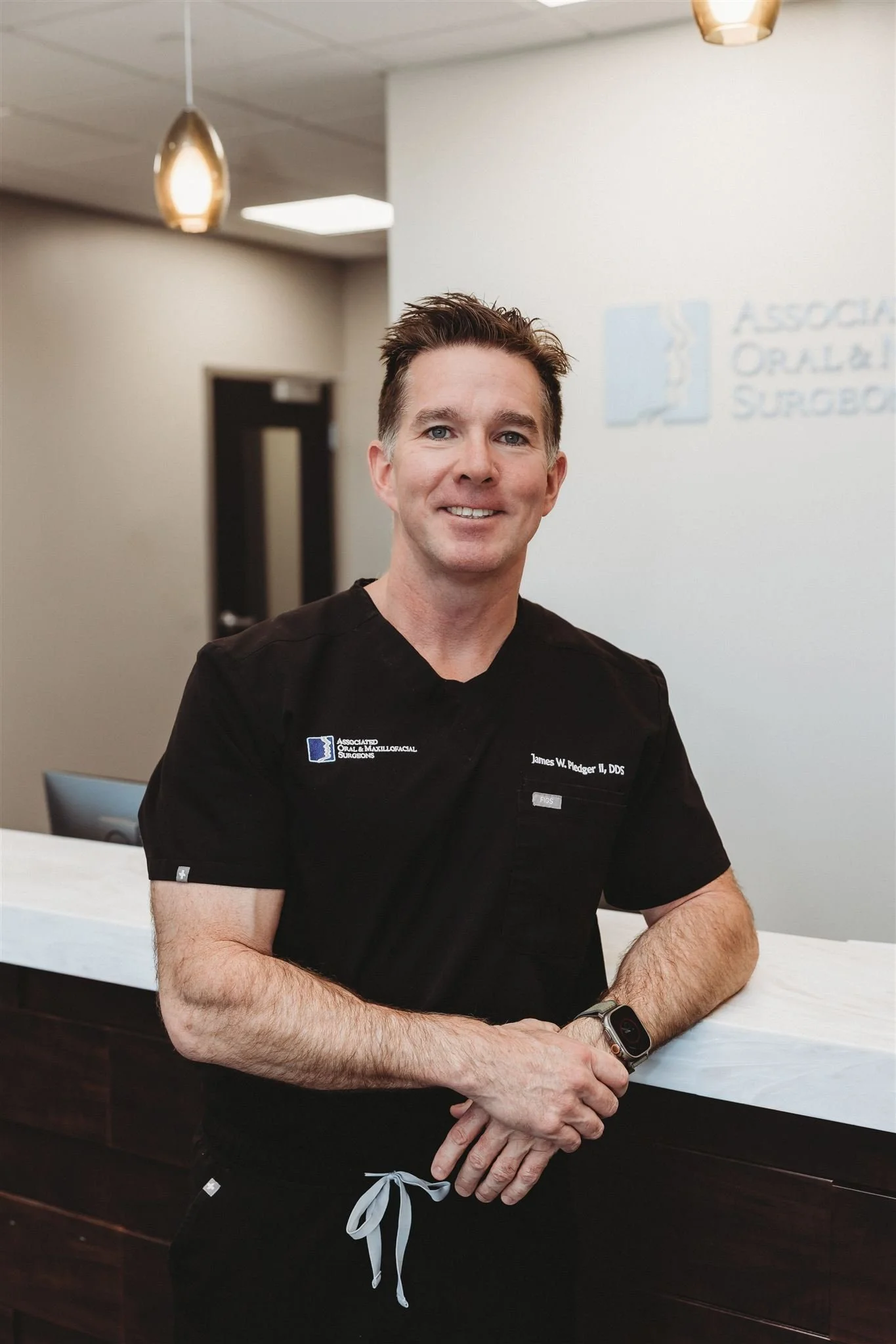 A male dental professional in a black uniform standing at a reception desk in a dental office.
