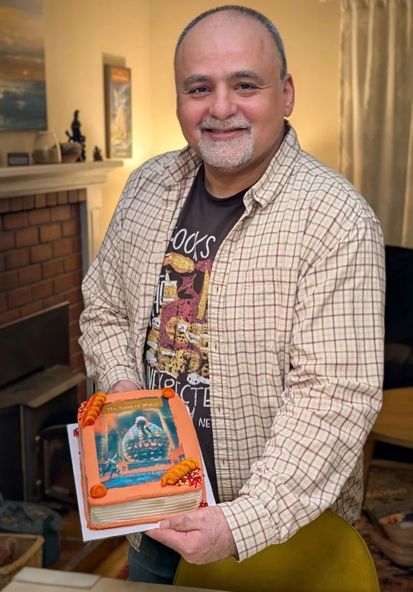 Samer Rabadi holding a birthday cake featuring the cover of Eight 5: The Saint of Water
