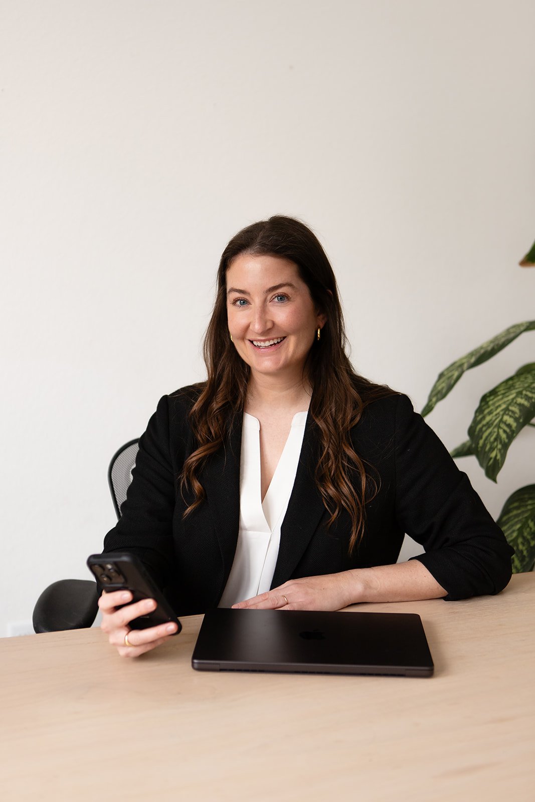 Marta de Movellan, founder of Studio Movellan, looks directly at the camera holding her phone in front of a laptop at a desk