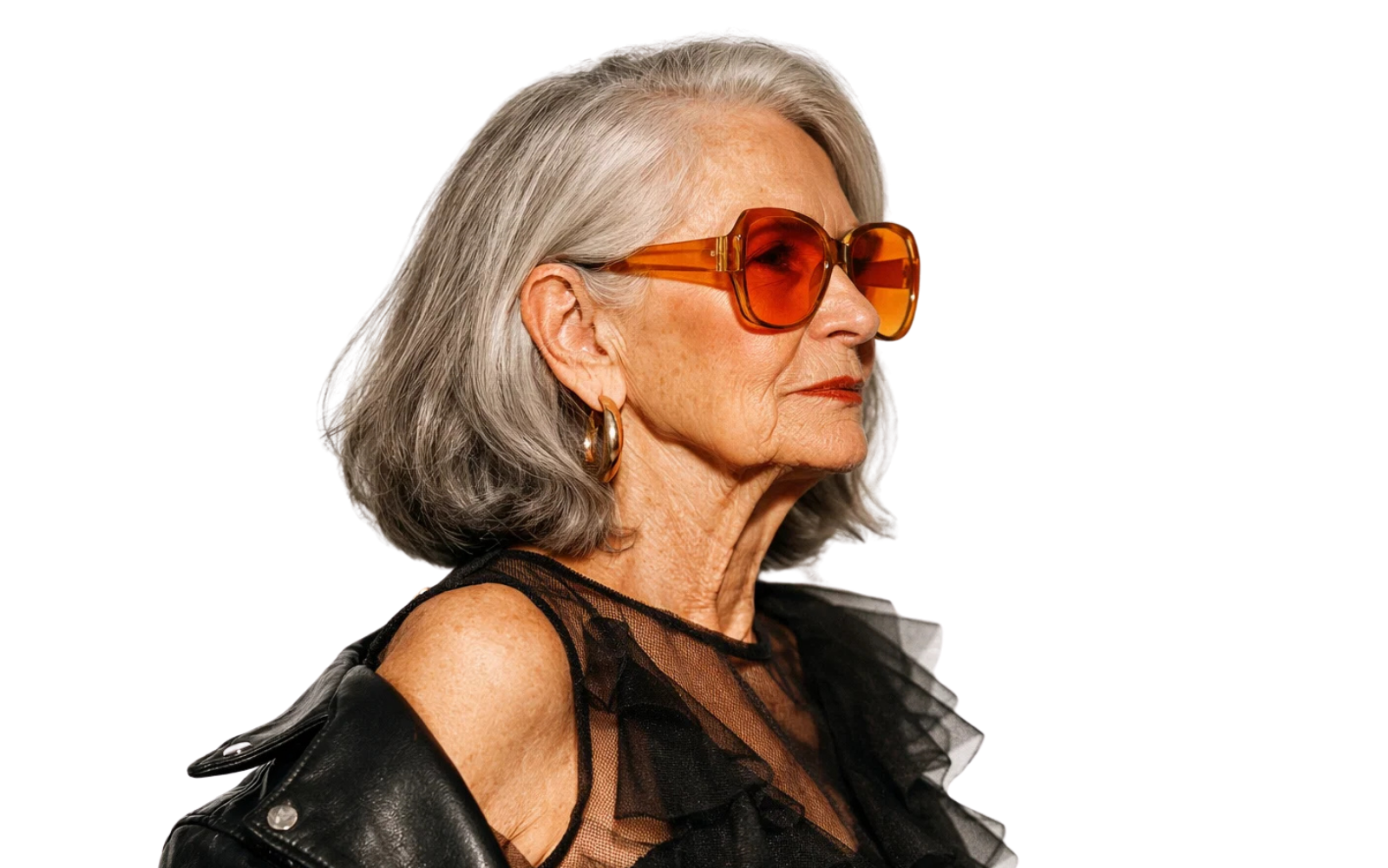 Ikoninen vanha nainen, jolla harmaat hiukset ja isohkot oranssit aurinkolasit, pukeutuneena mustaan mesh-toppiin ja nahkatakkiin.