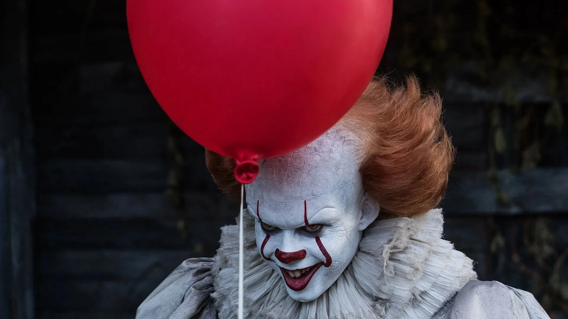 Pennywise grins while holding a red balloon