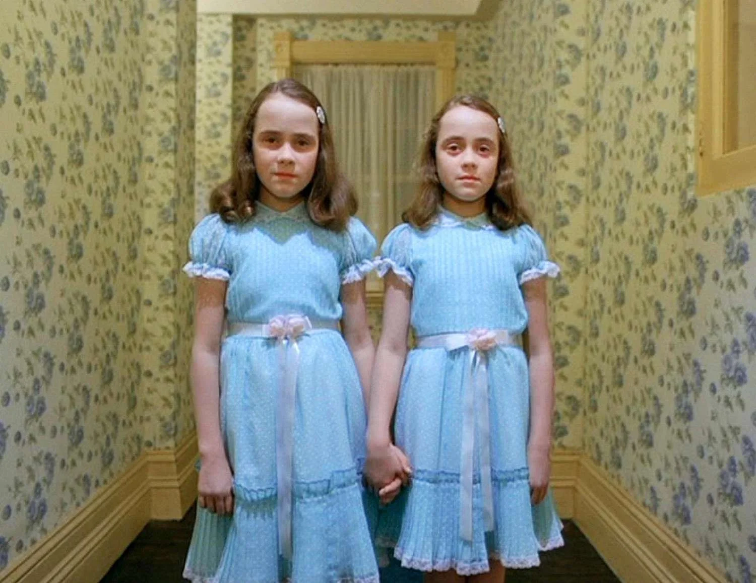 The Grady sisters from The Shining stand in matching blue dresses and hold hands