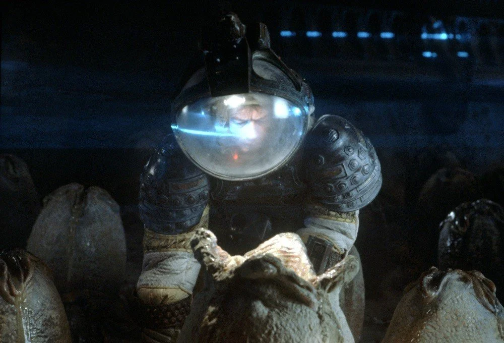 From the movie Alien, a person in a space suit looks down at an egg that is beginning to open.