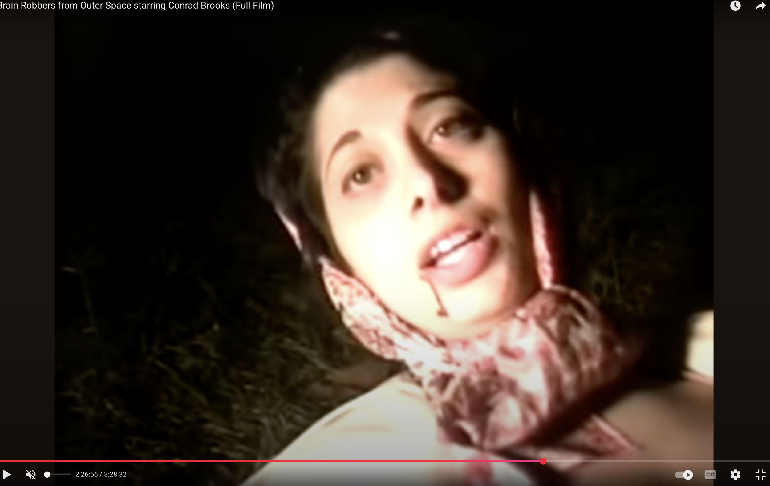 Screenshot from the movie Grave Robbers from Outer Space that shows a woman in a headscarf and overcoat with a trickle of blood coming from the corner of her lip