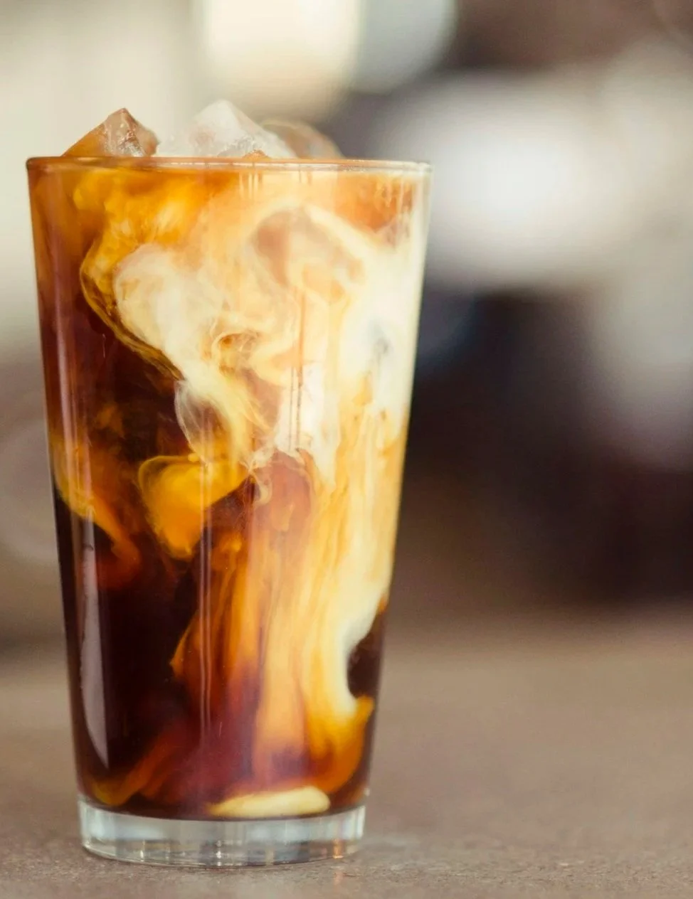 A tall glass of iced coffee with cream swirling in the dark coffee, creating a marbled effect.