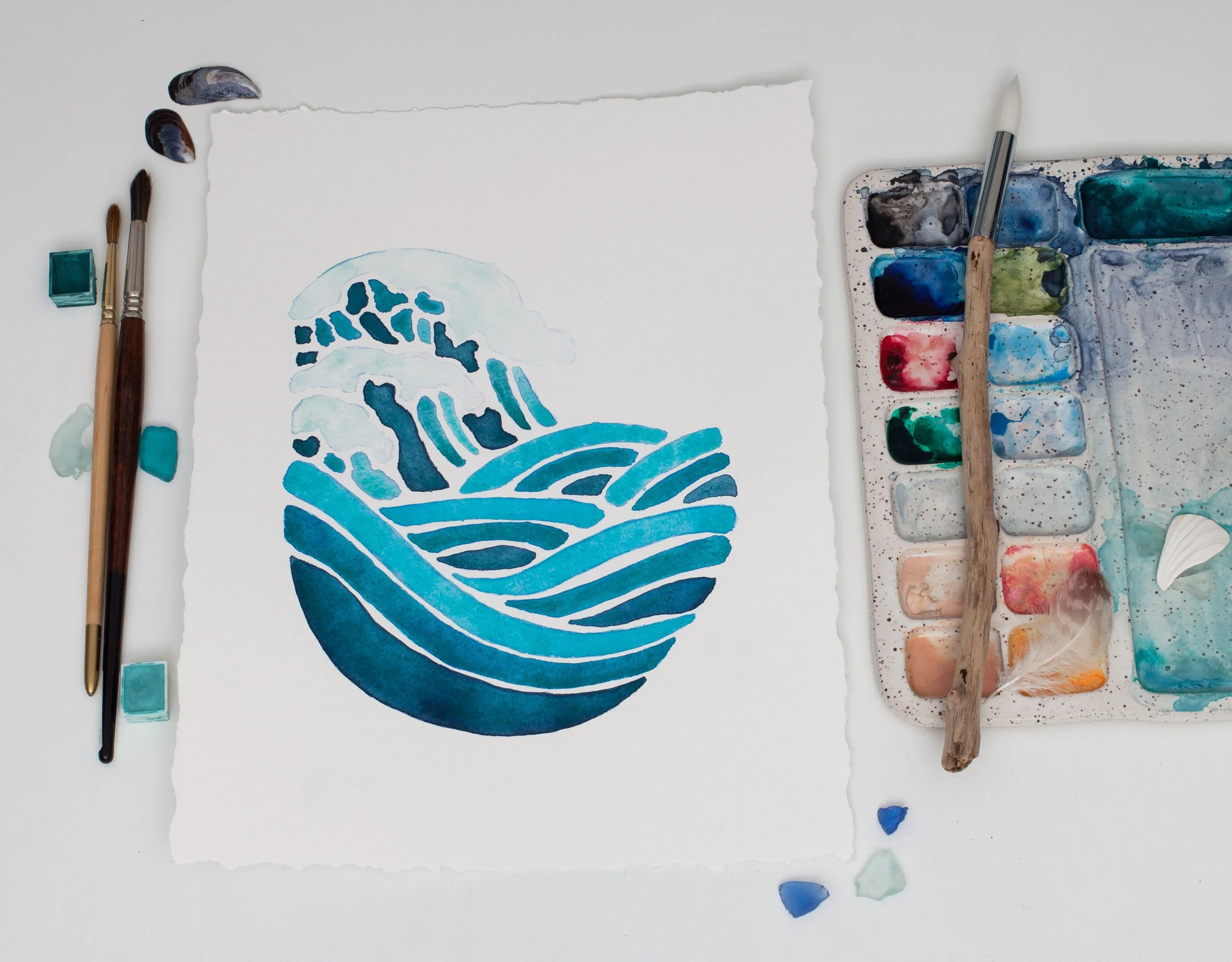 “Modern Waves” watercolor artwork on artist’s table beside brushes and a watercolor palette, showcasing its rich blue tones and organic textures.
