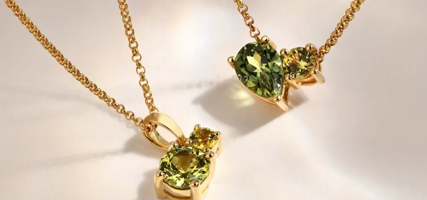 Gold necklaces with green gemstone pendants, featuring a heart-shaped stone and round stones set in gold.