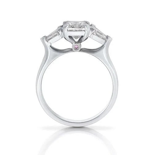 Close-up of a White gold engagement ring with a large central diamond and a small pink gemstone underneath the setting.