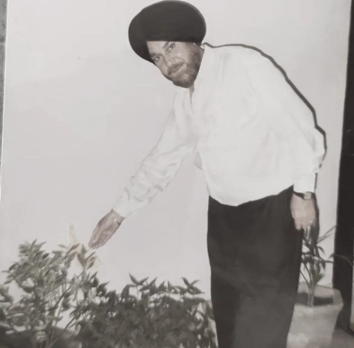 A man wearing a turban and a white shirt, gesturing towards plants in a garden.