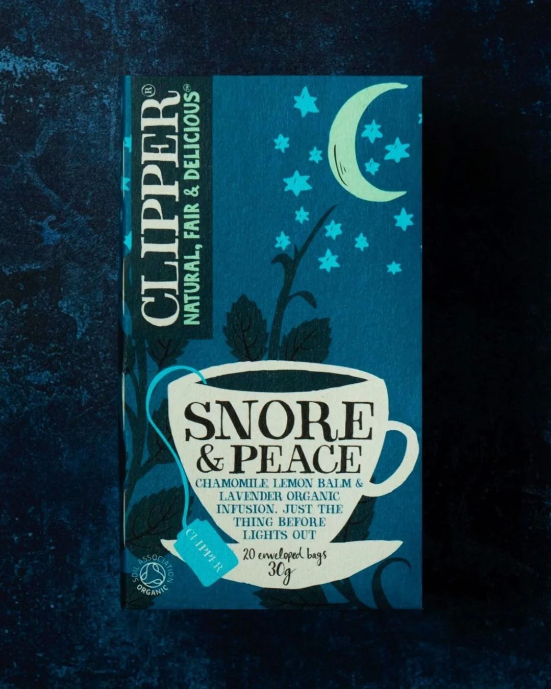 Box of Clipper Tea, Snore & Peace flavor, chamomile, lemon balm, and lavender organic infusion, 20 tea bags, 30 grams, with a dark blue background and moon and stars illustration.